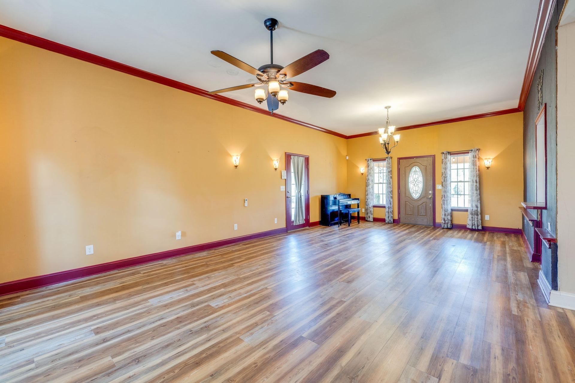 Empty living room with wood floors, yellow walls, ceiling fans, and large windows.