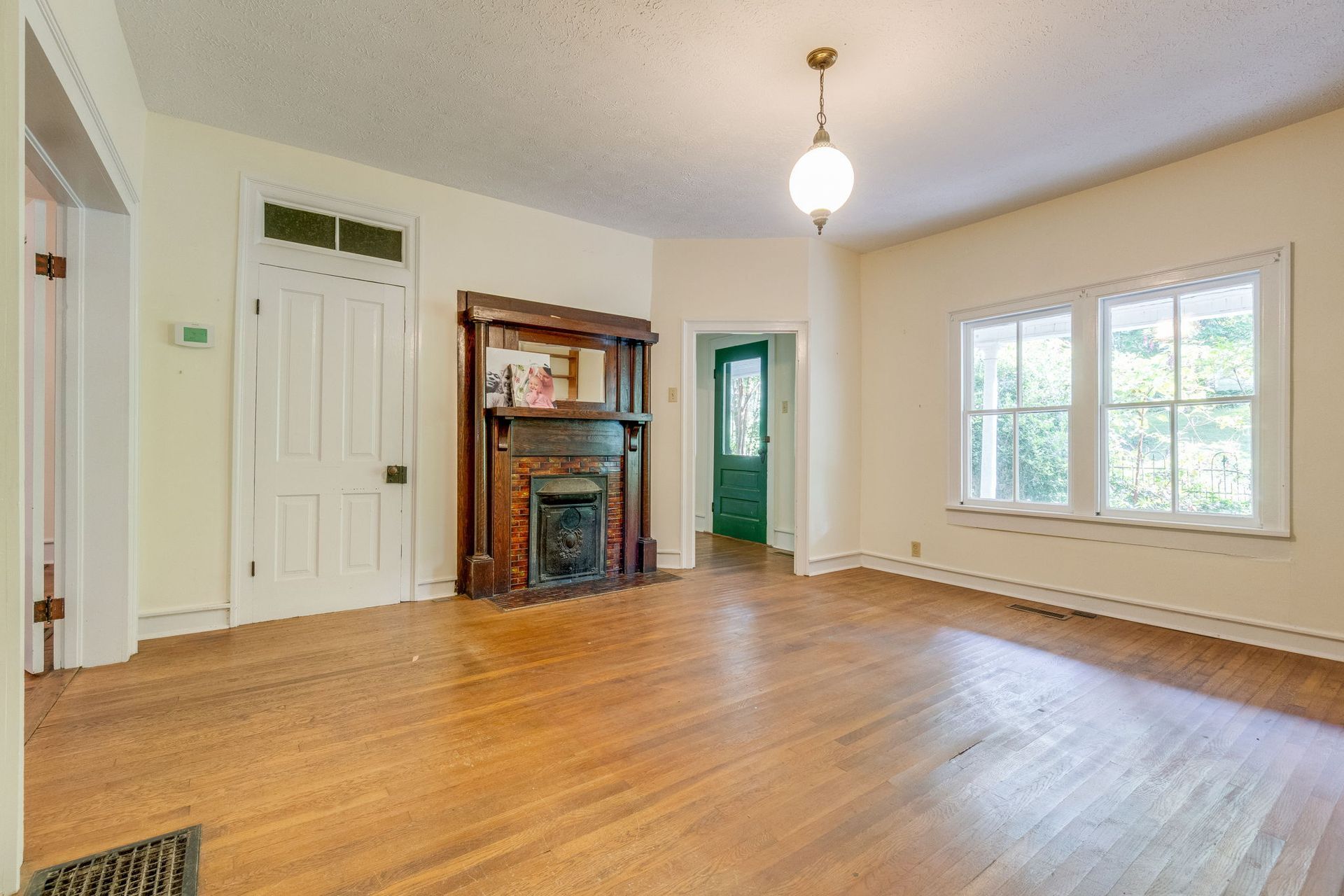 Empty living room with hardwood floors, fireplace, green door, and large front window