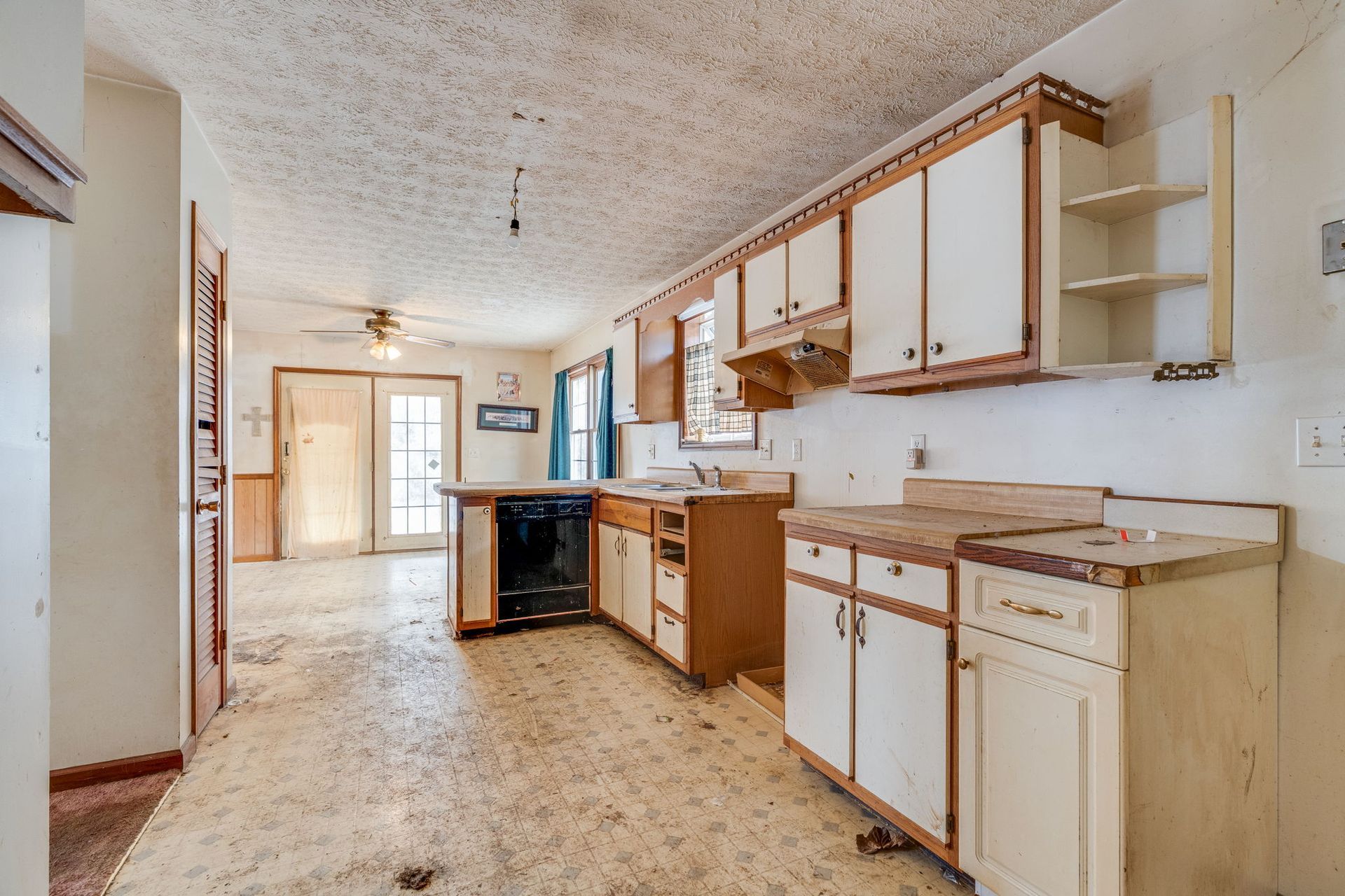 Dilapidated kitchen with worn cabinets, stained countertops, and damaged floor.