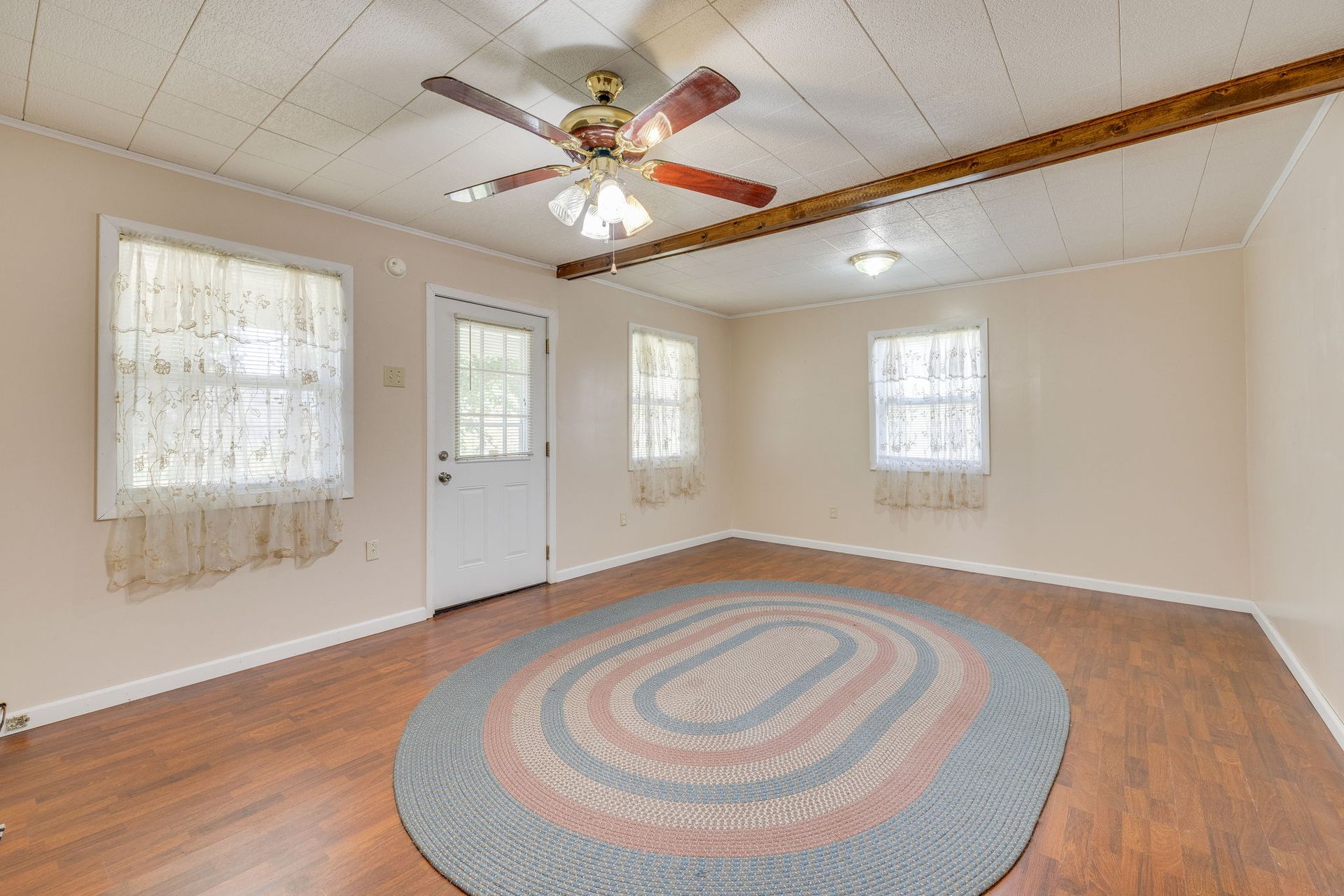 Empty living room with hardwood floors, ceiling fan, white walls, and a round rug near the center.