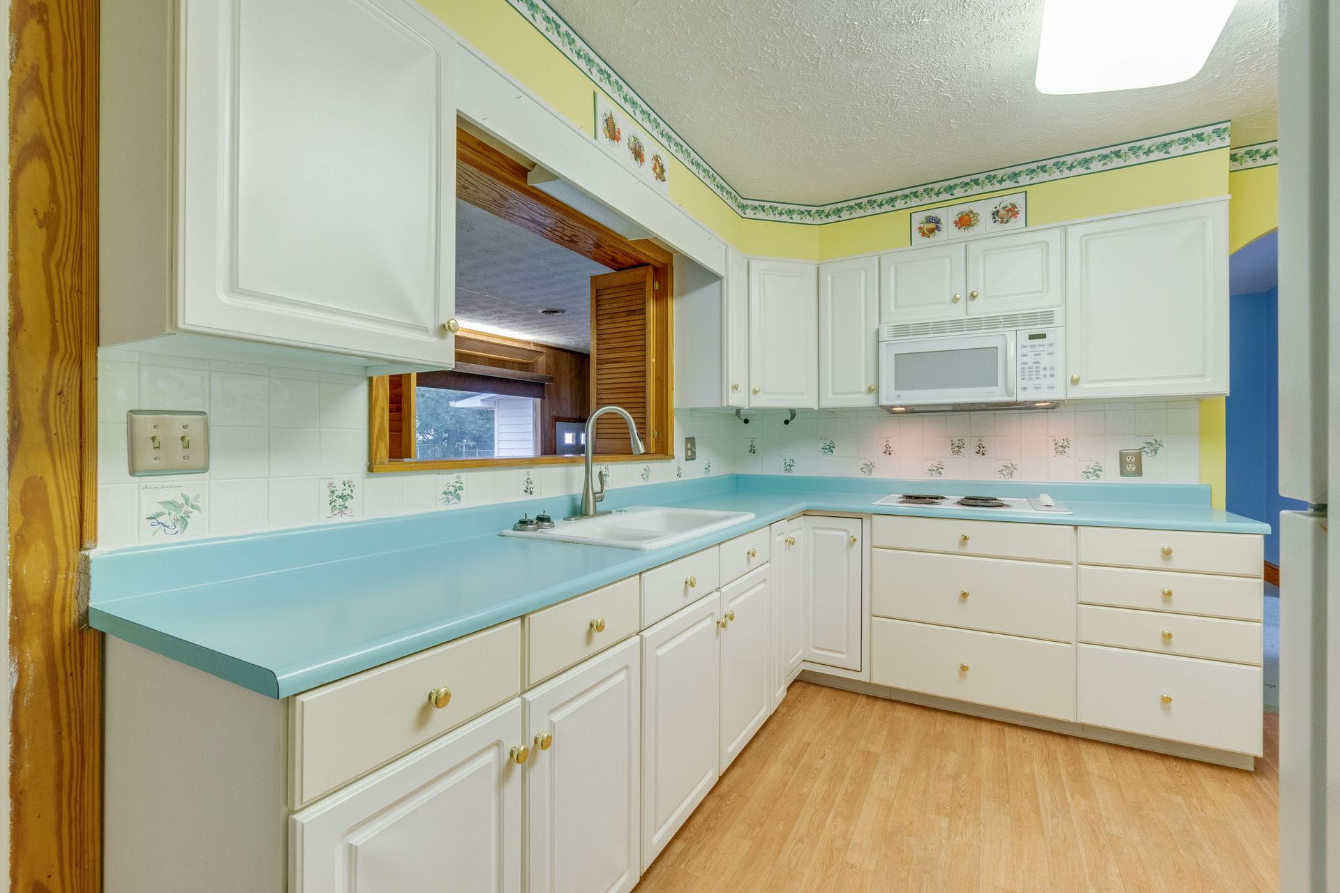 Bright kitchen with white cabinets, aqua countertops, and a sink under a window