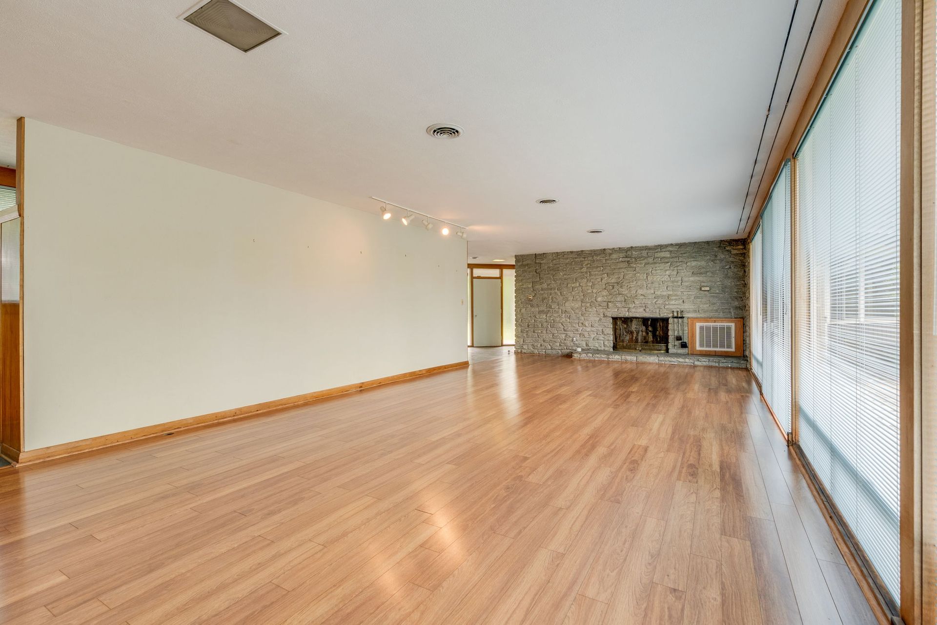Empty living room with hardwood floors, stone fireplace, and large sliding glass doors