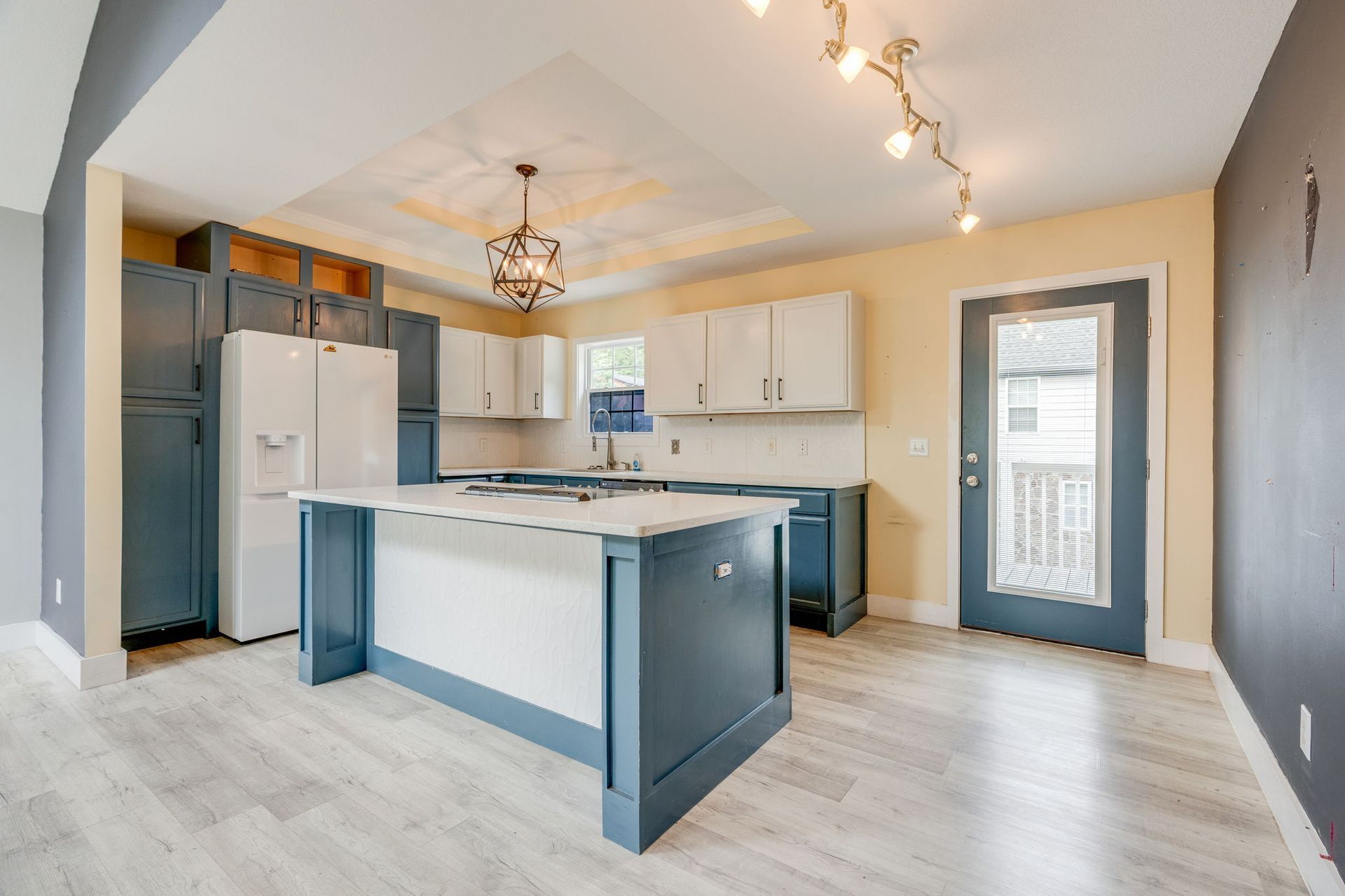 Bright modern kitchen with white cabinets, gray island, stainless appliances, and wood-look flooring.
