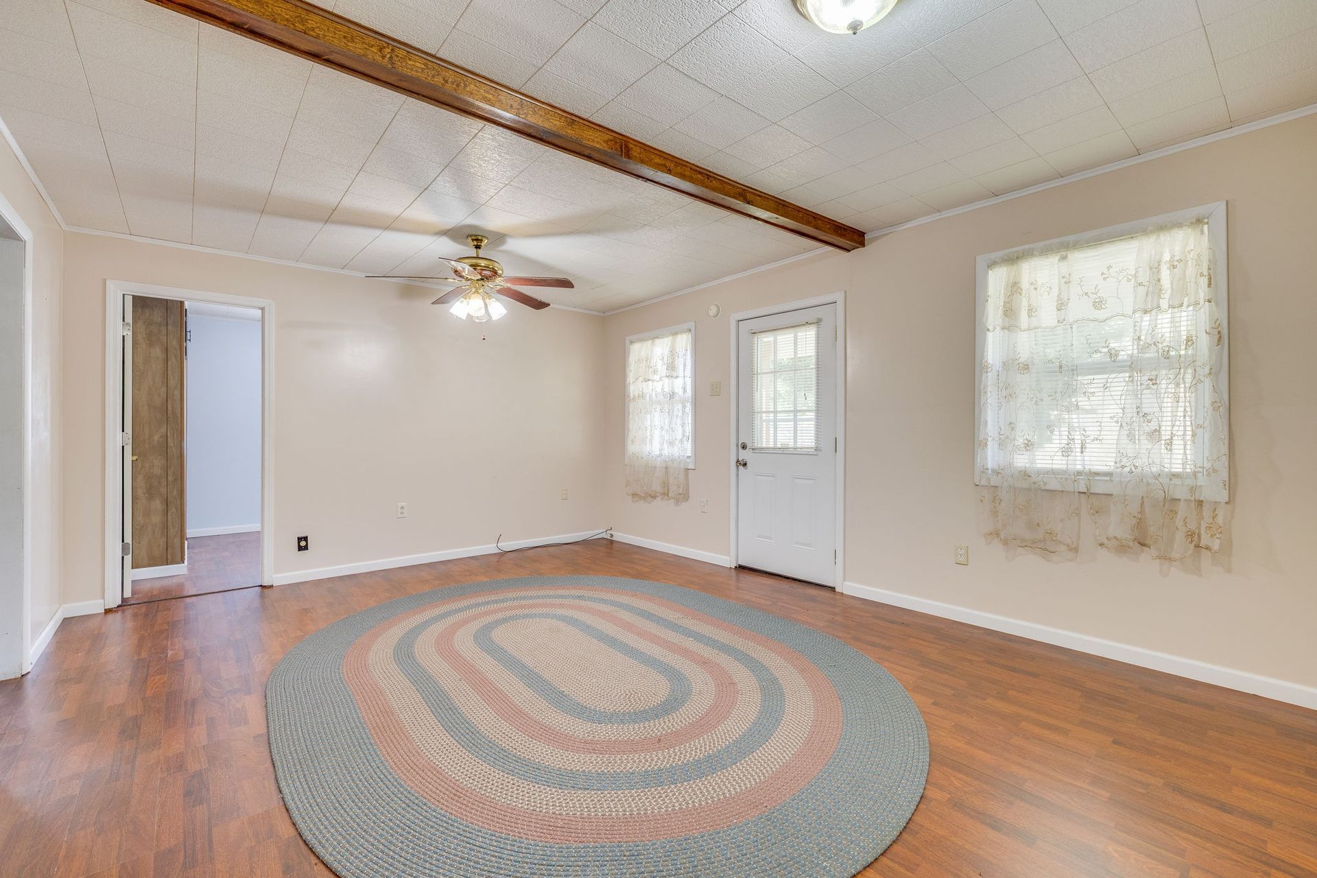 Empty living room with wood floors, round rug, ceiling fan, and two windows by a white front door