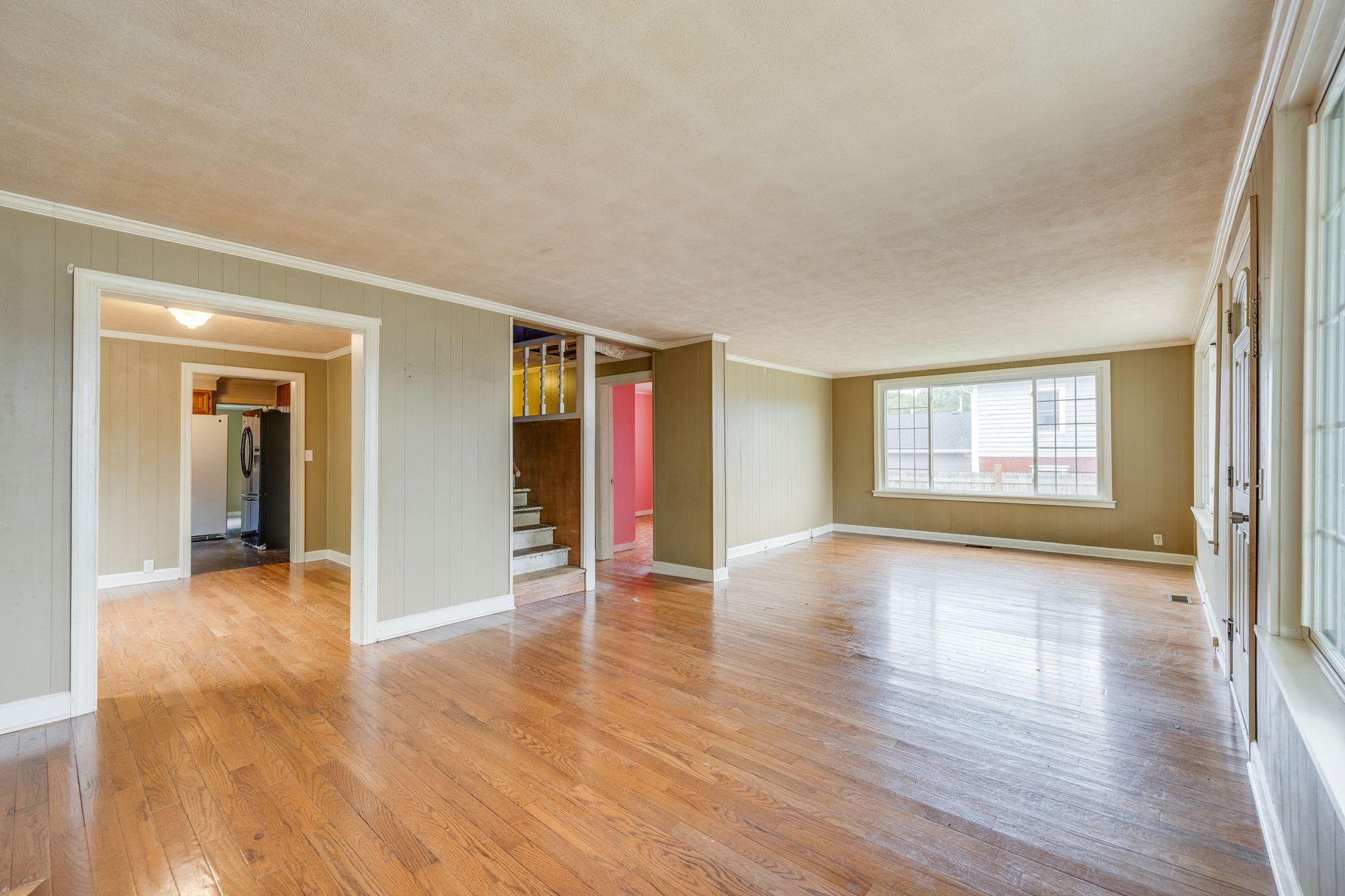 Empty living room with hardwood floors, beige walls, and large windows