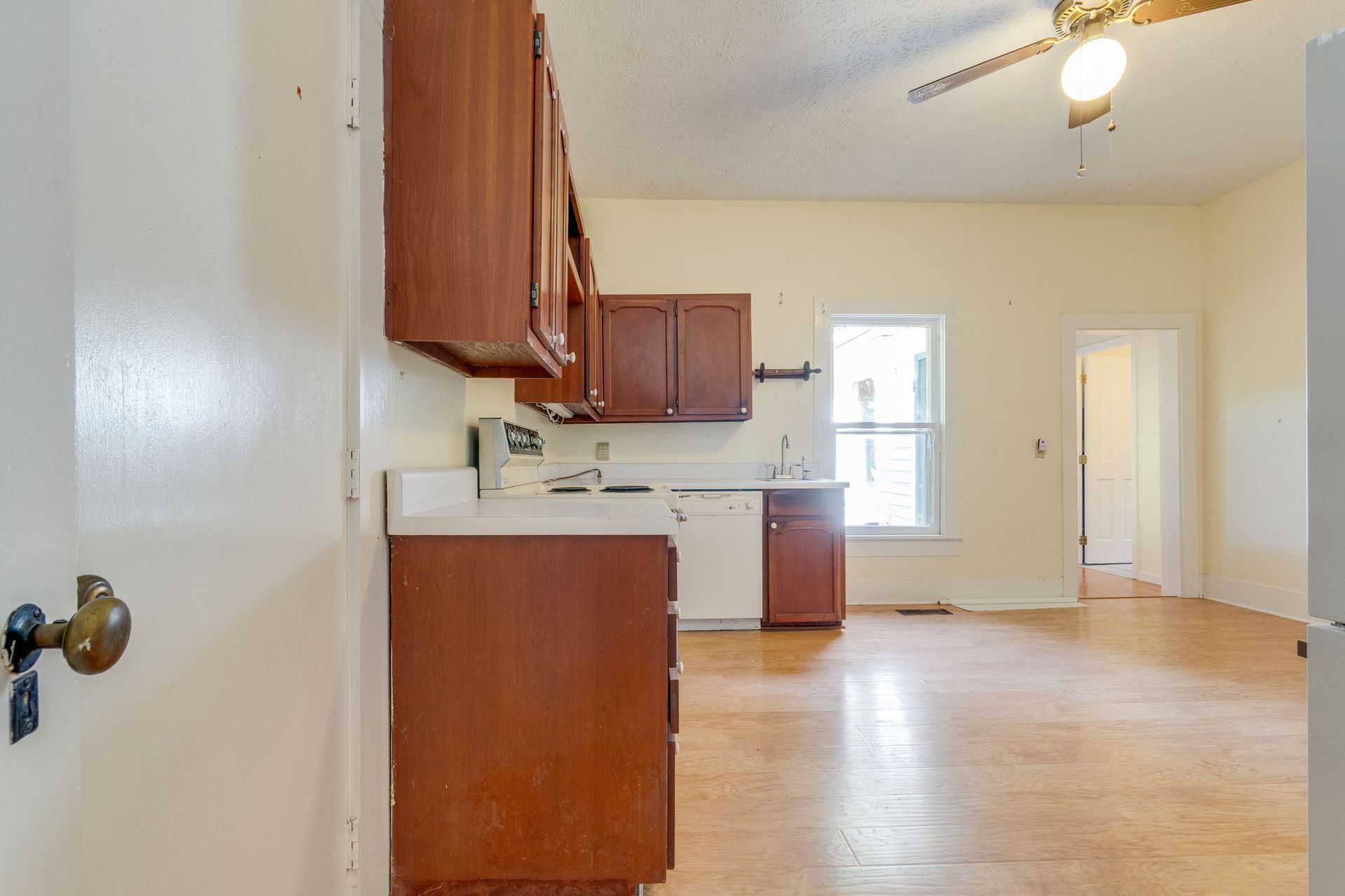 Empty kitchen with wooden cabinets, light wood floor, ceiling fan, and bright windowed dining area