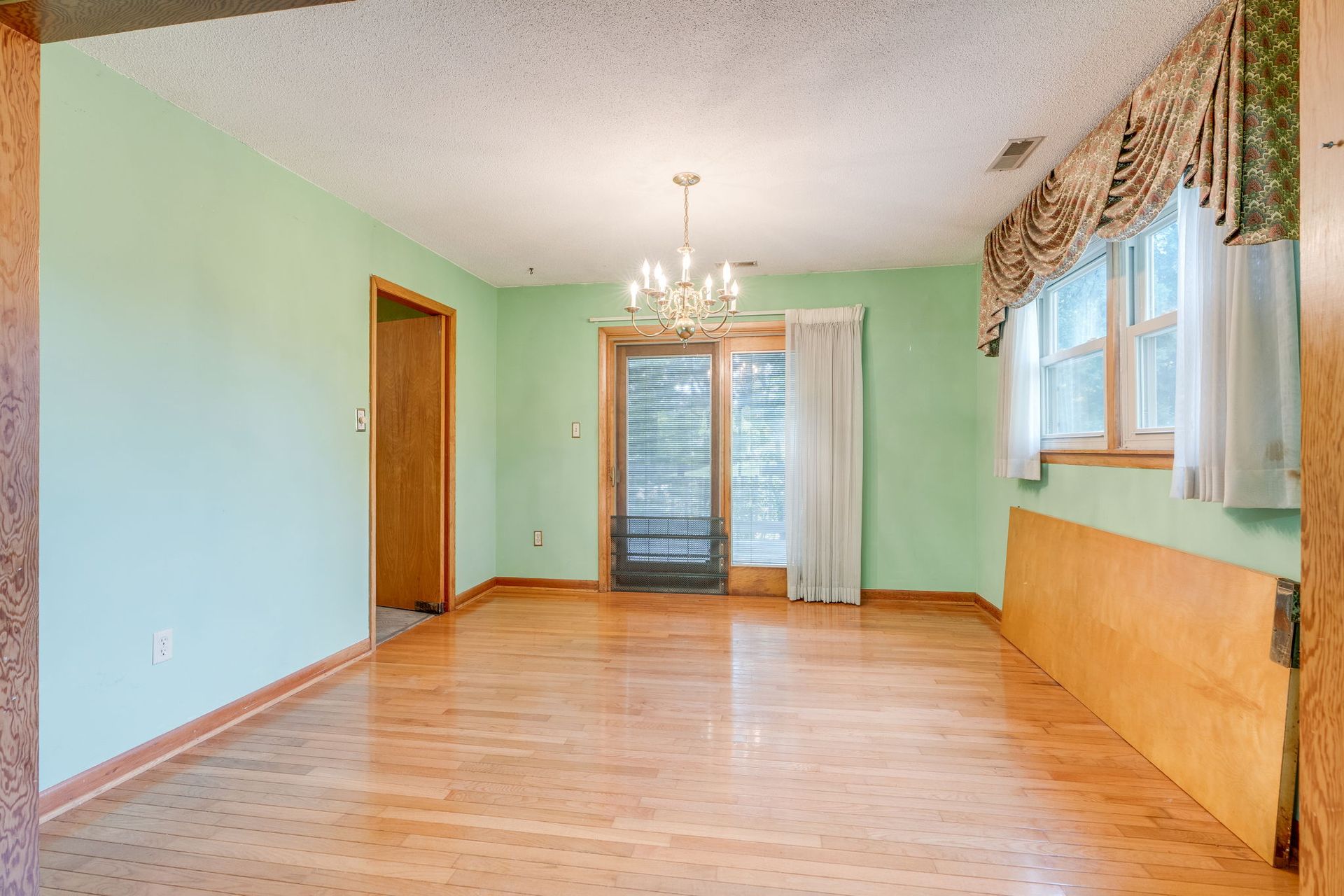 Empty mint-green living room with hardwood floor, chandelier, and sliding glass door to a balcony