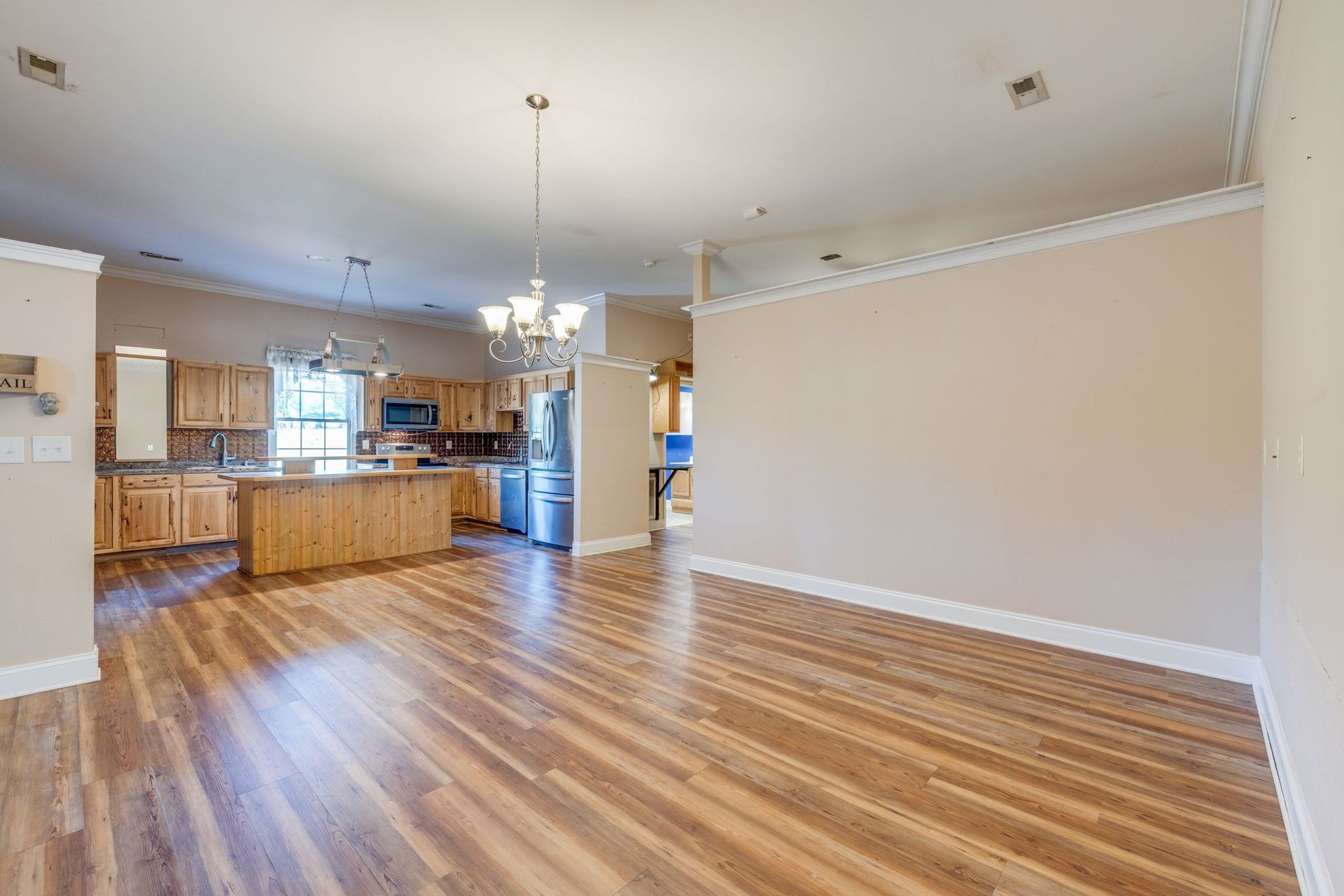 Empty open-plan living room with hardwood floors and kitchen, beige walls, and ceiling lights