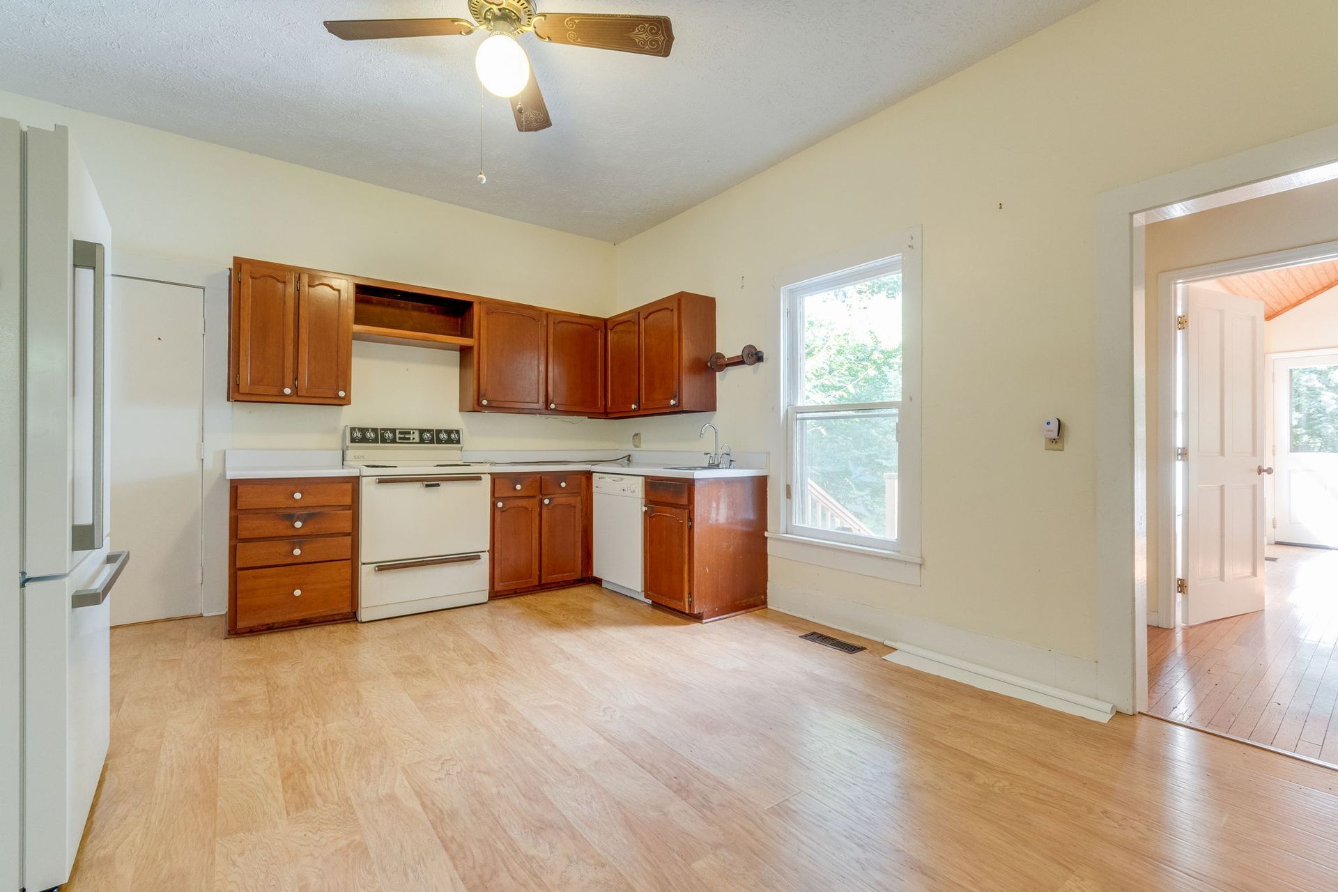 Bright empty kitchen with wood cabinets, white appliances, and light wood floors