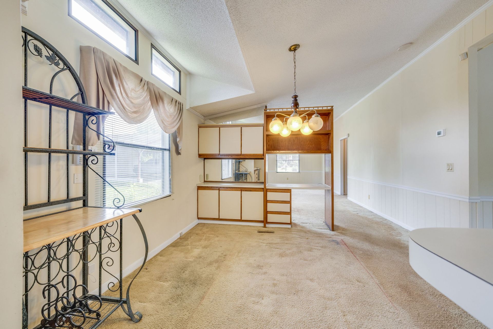 Empty carpeted room with built-in shelves, a window with sheer curtains, and a hanging light fixture
