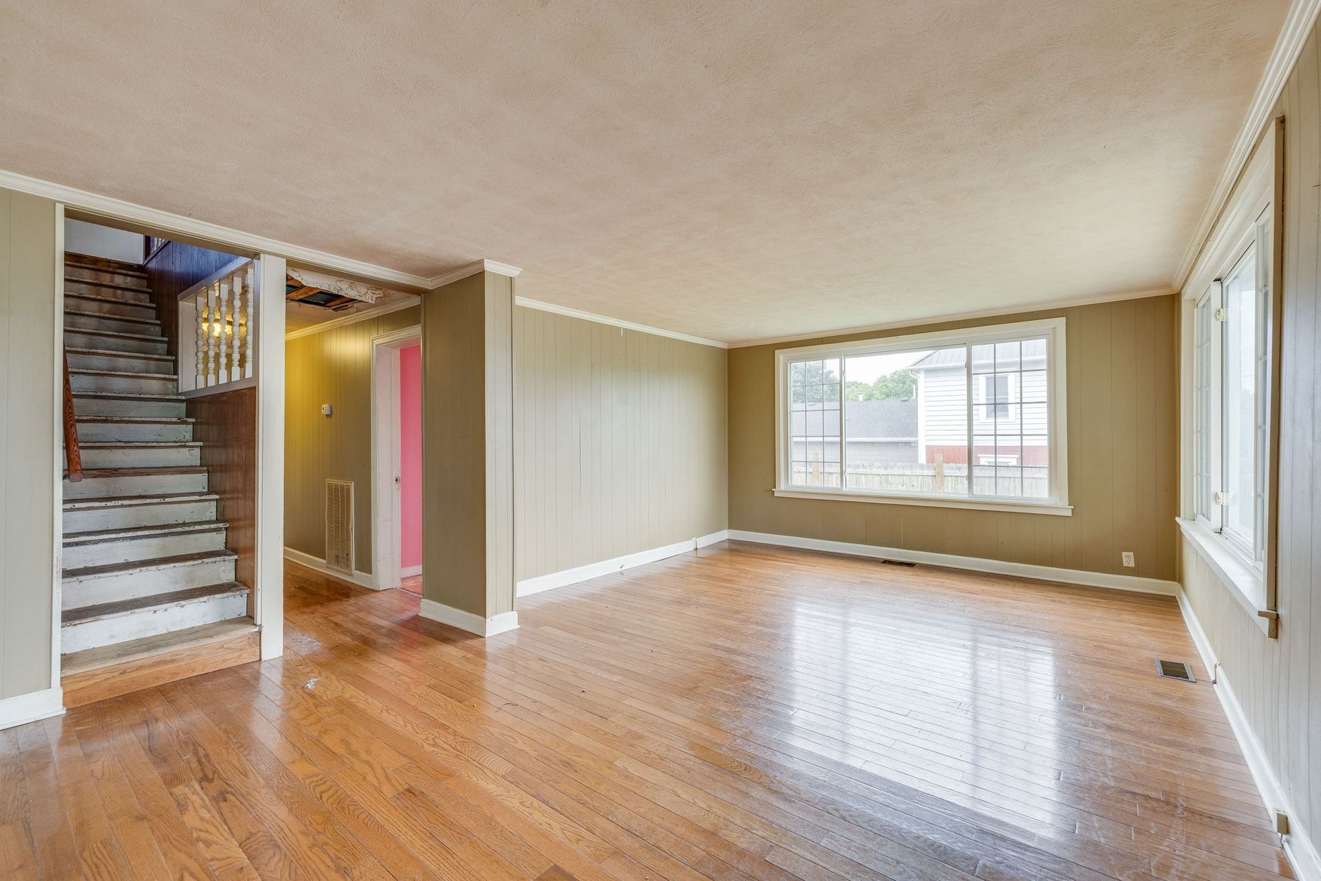Empty living room with hardwood floors, staircase, and large window letting in daylight