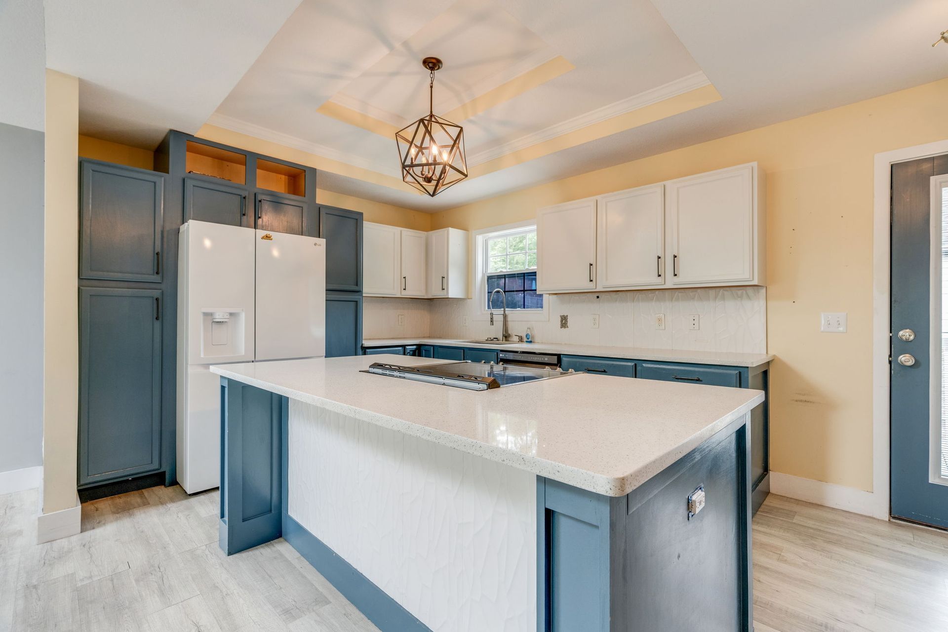 Bright modern kitchen with blue island, white cabinets, stainless fridge, and pendant light