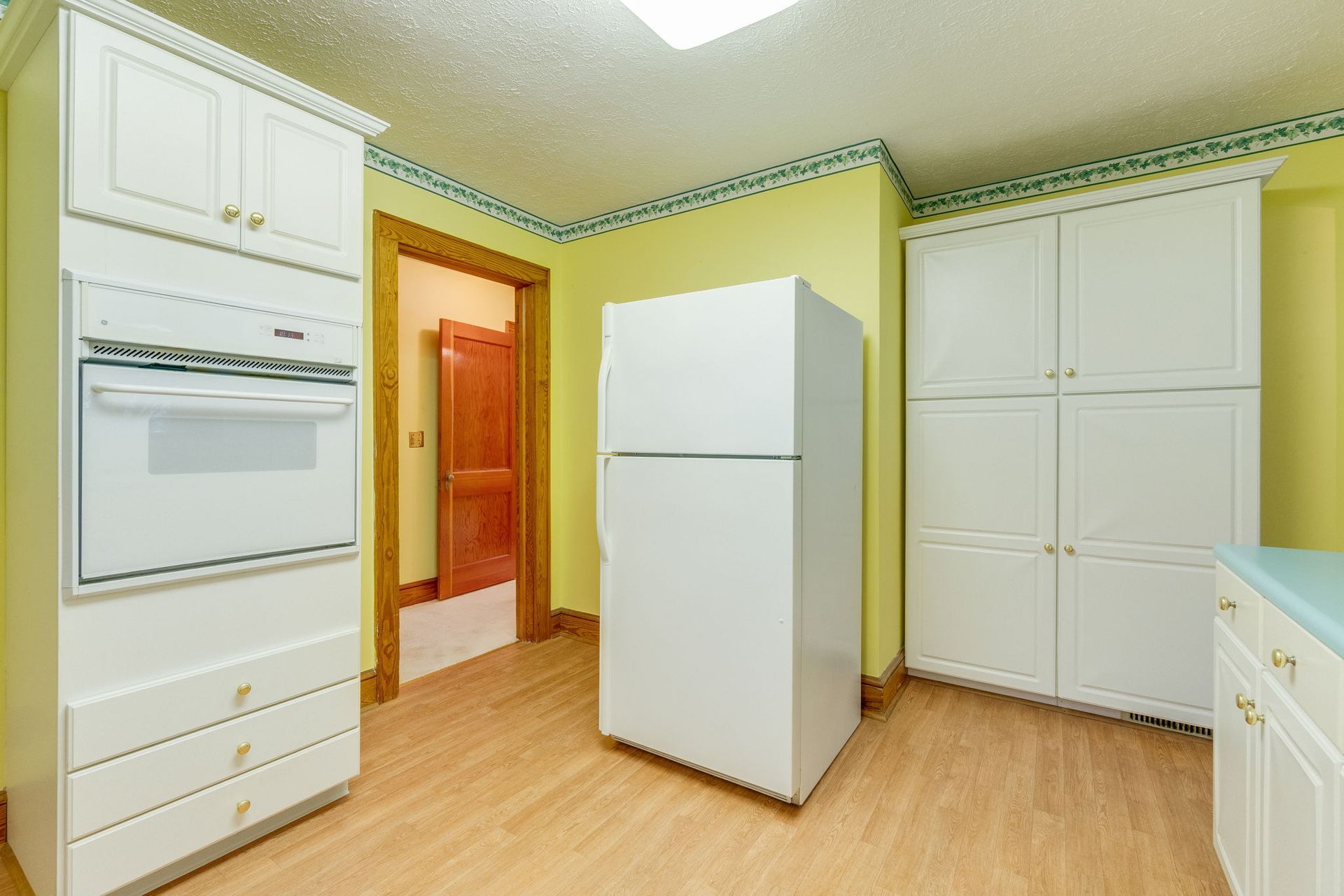 Empty white kitchen with built-in oven, refrigerator, and cabinets on wood flooring