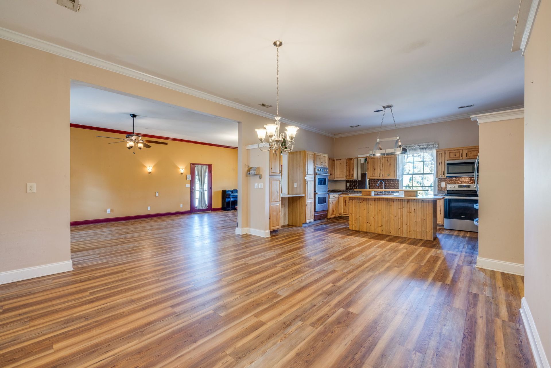 Open-plan living room with hardwood floors, beige walls, and a kitchen island in the background.