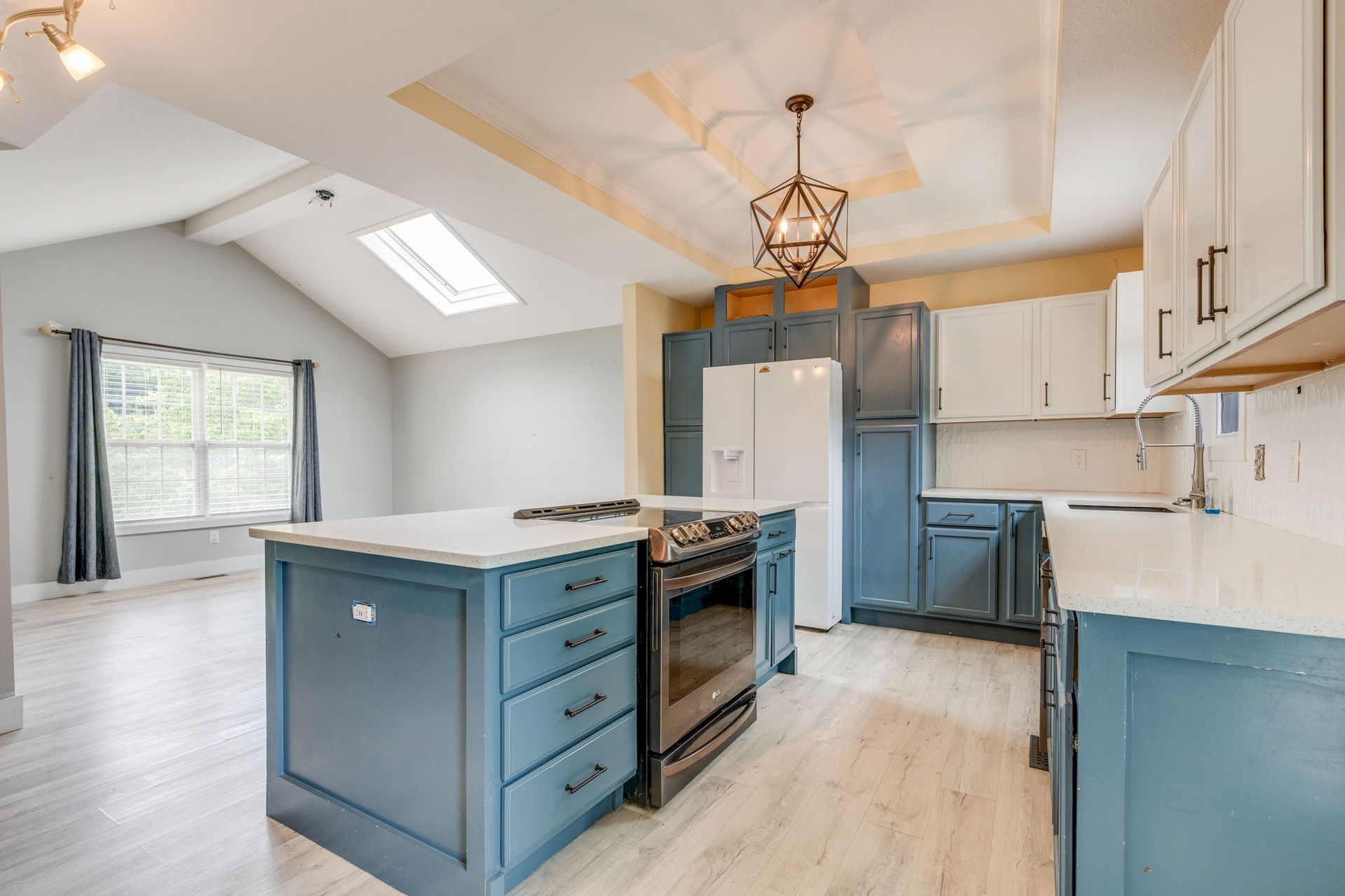 Bright modern kitchen with blue island, stainless appliances, white cabinets, and skylight windows
