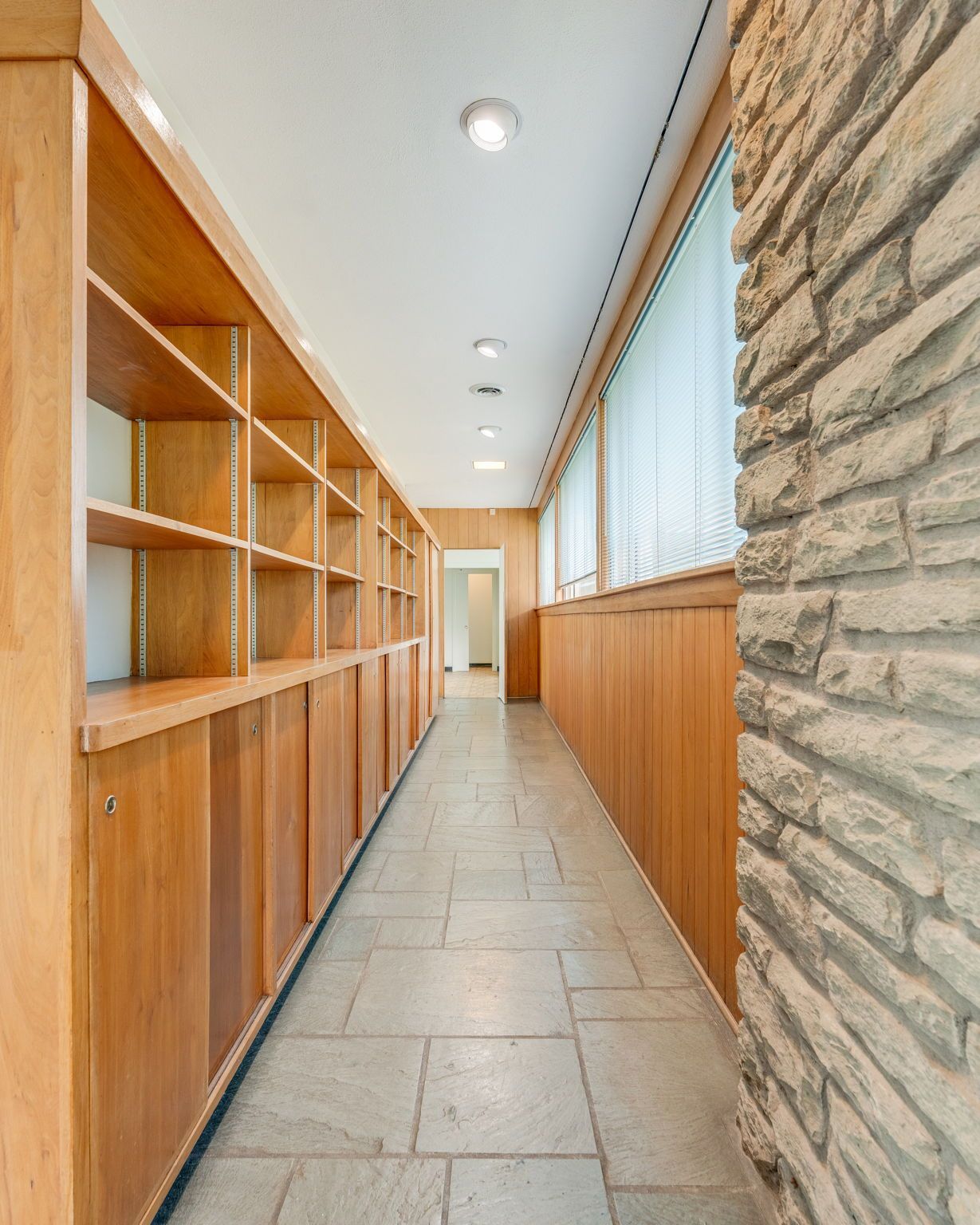 Modern hallway with wood cabinets, stone wall, tile floor, and recessed ceiling lights