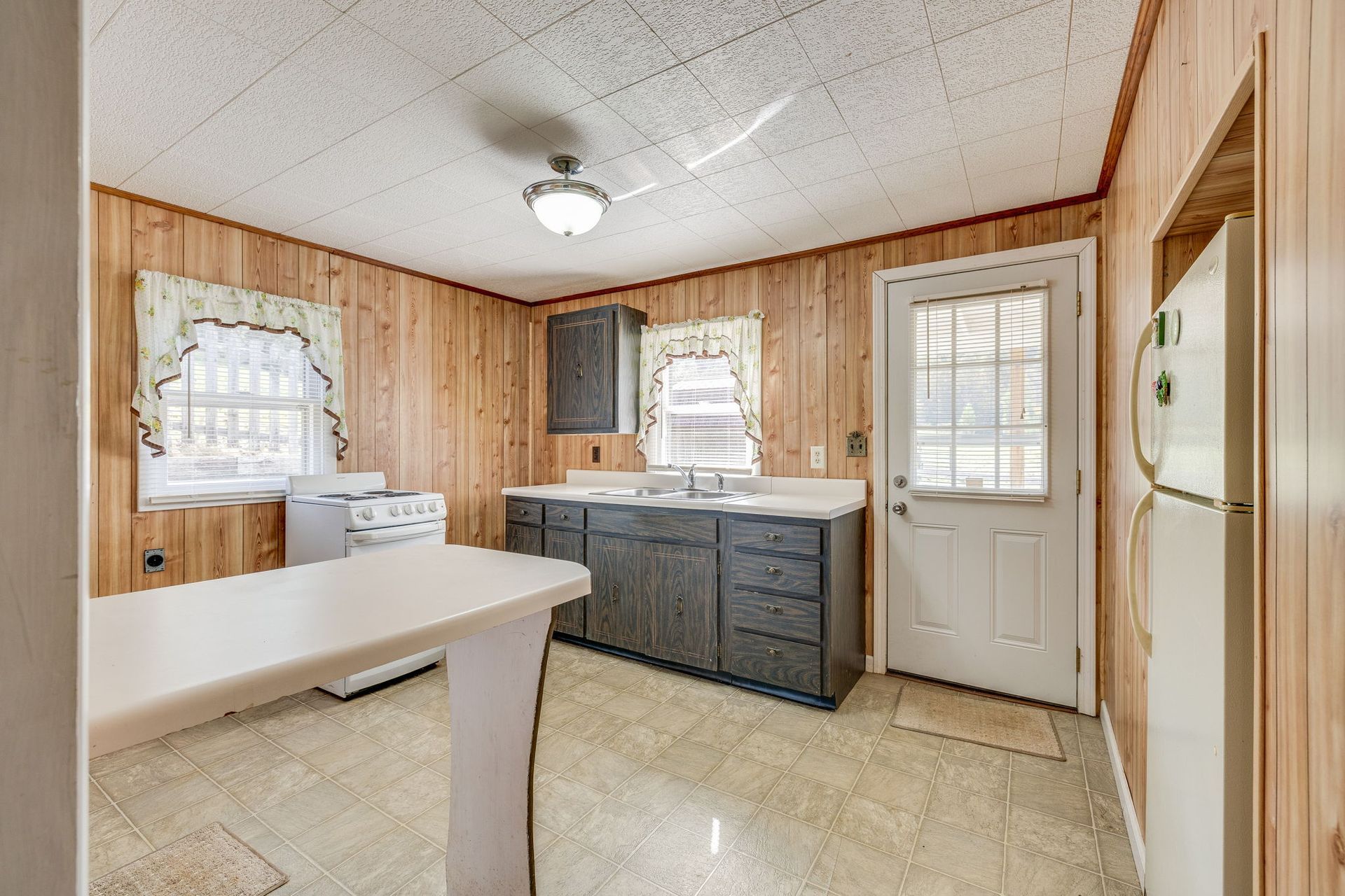 Laundry room with washer and sink, wood-paneled walls, tile floor, and a door with blinds.
