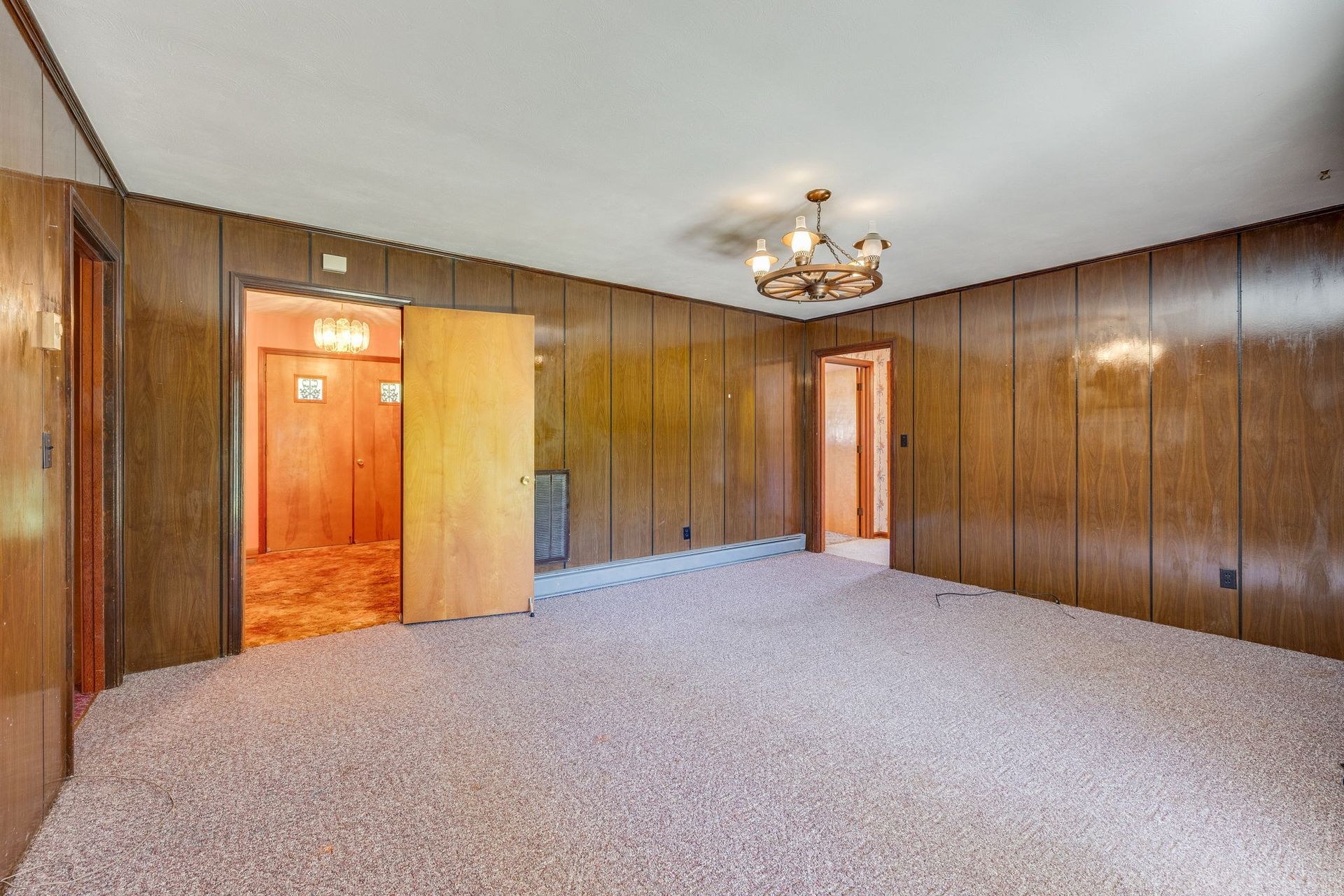 Empty wood-paneled room with carpet, a ceiling light, and two open doorways.