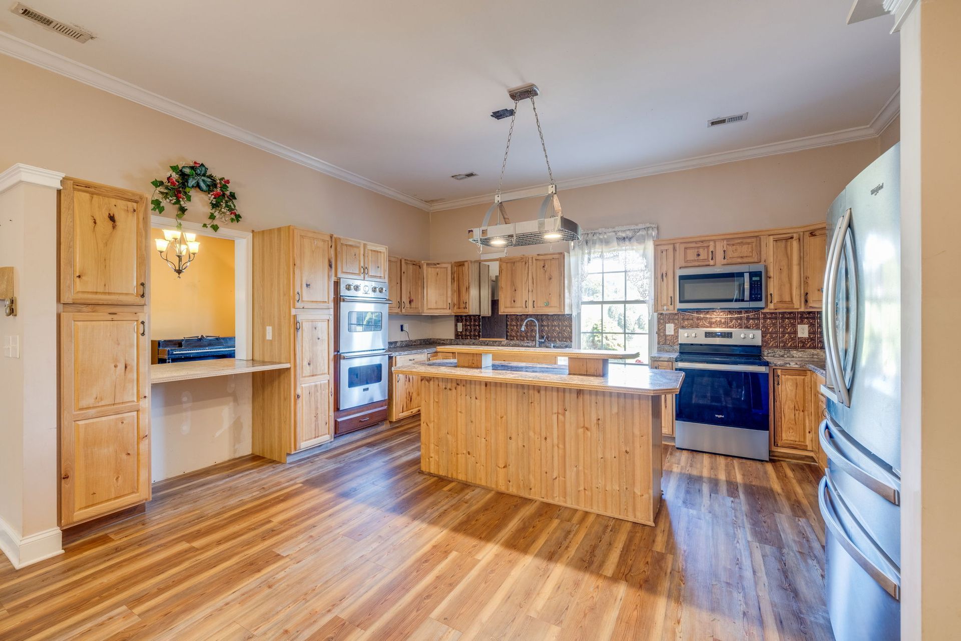Bright modern kitchen with wooden cabinets, island, stainless steel appliances, and hardwood floors.