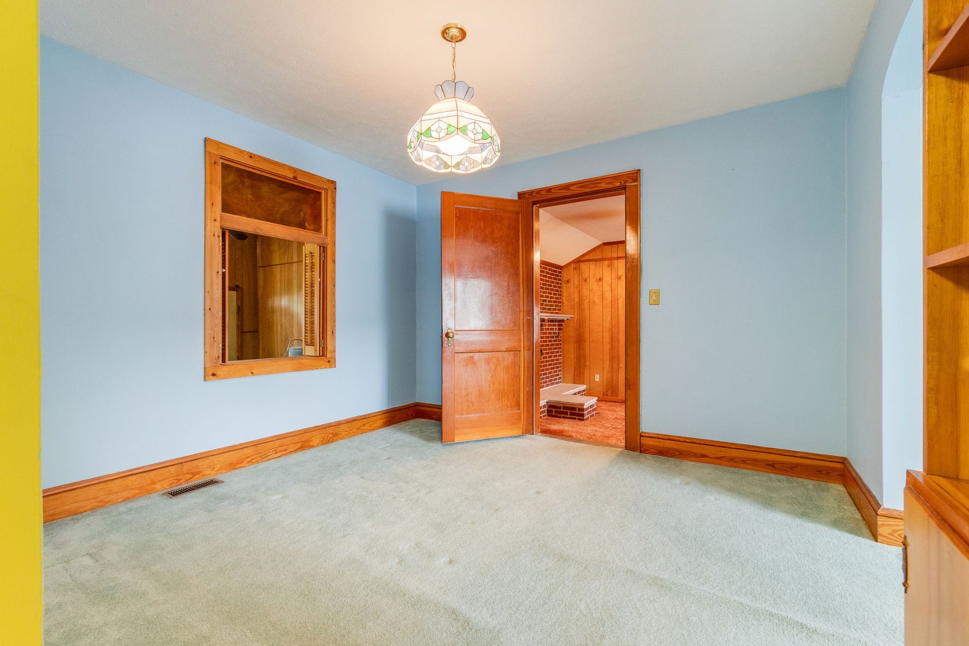 Empty light-blue bedroom with mirrored closet, open wooden door, and carpeted floor