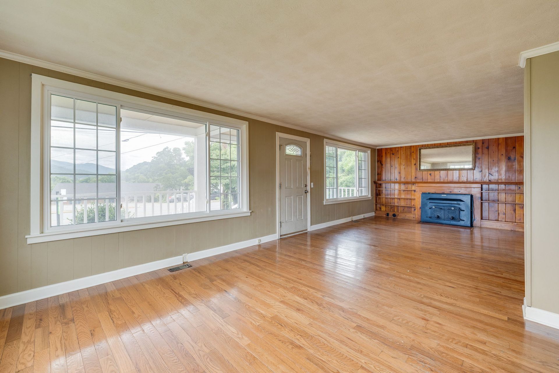 Empty living room with hardwood floors, large windows, and a blue fireplace mantel