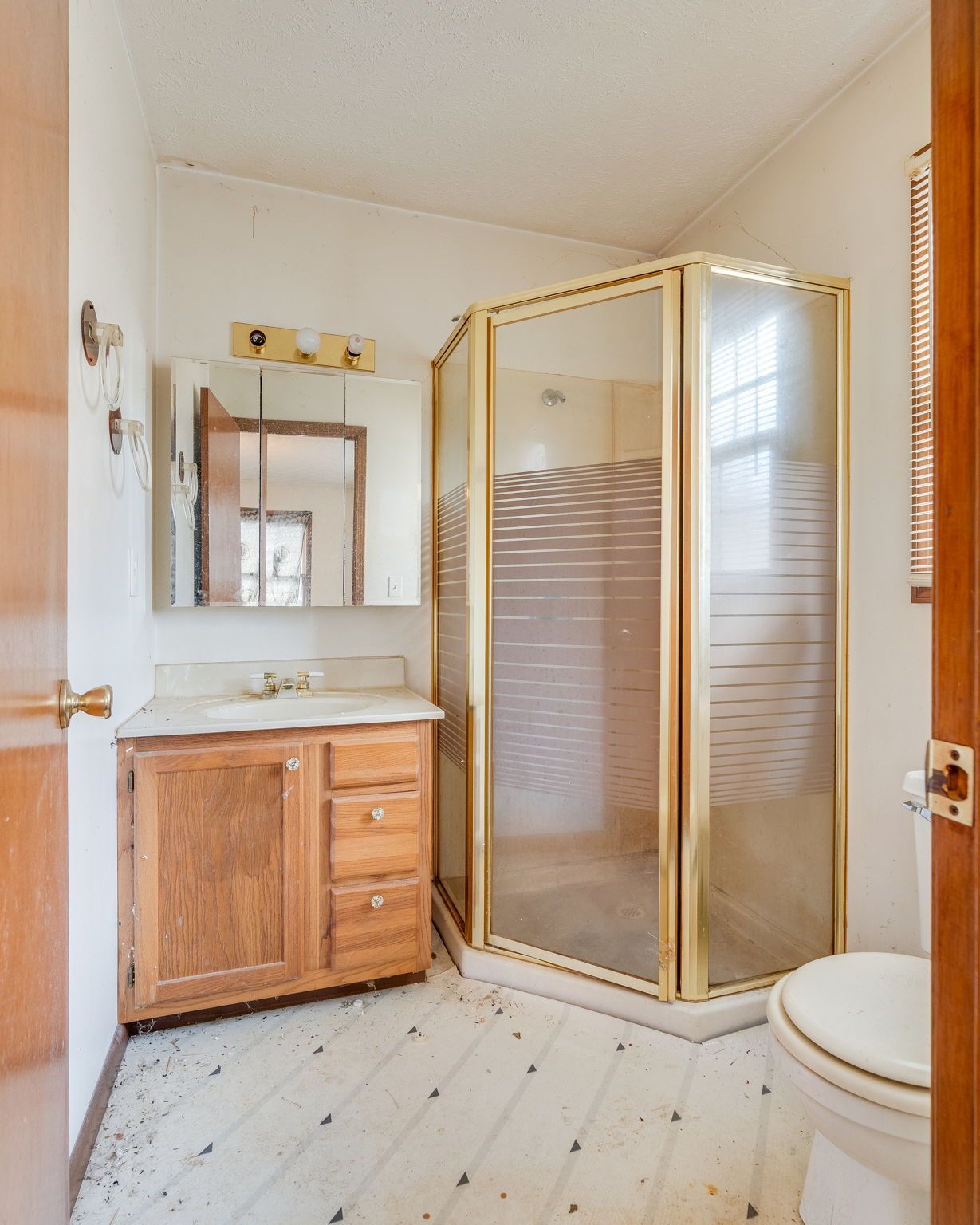 Bathroom with a wooden vanity, a golden-framed shower, and a white toilet. White and gray tiled floor.