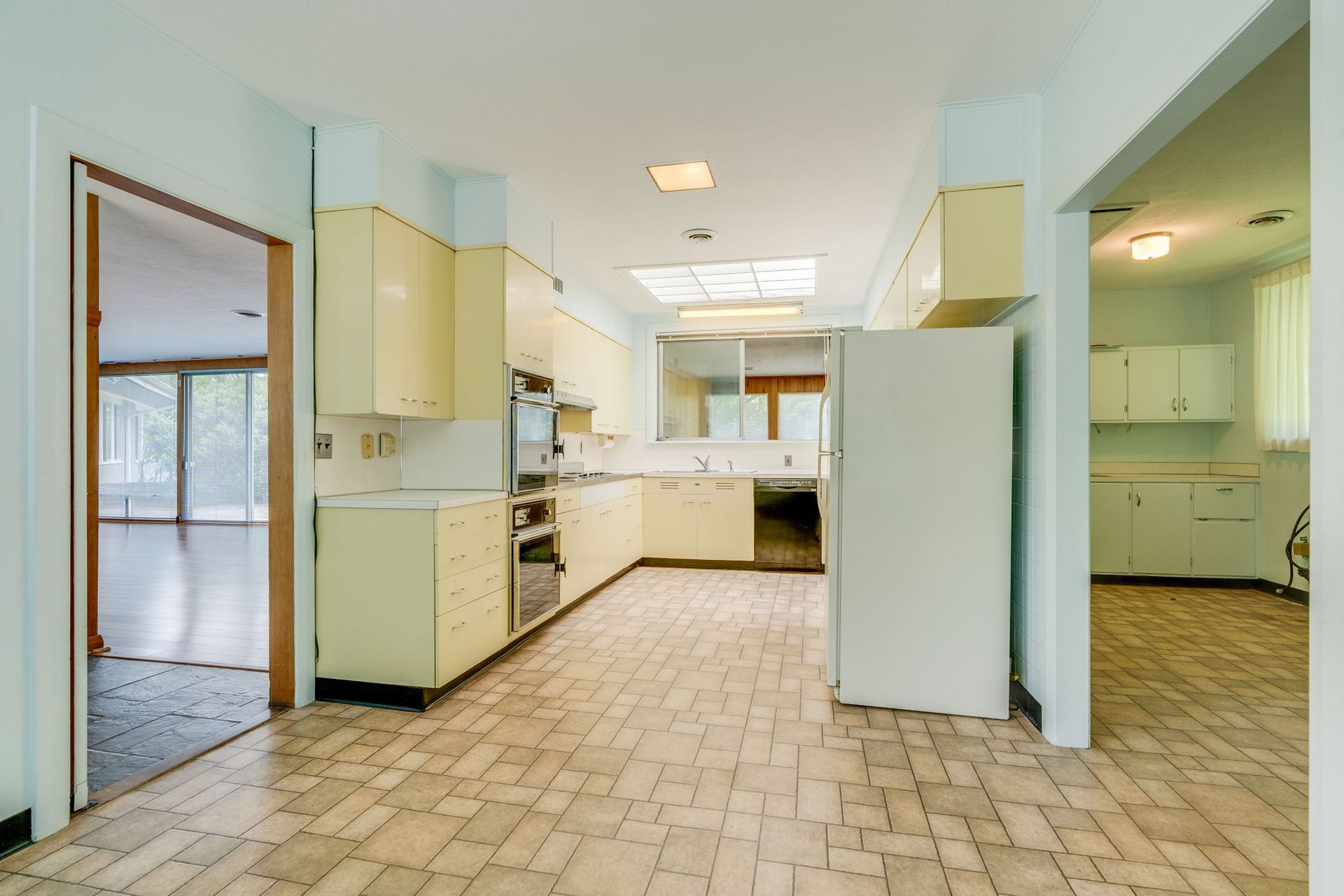 Empty pale-yellow kitchen with white appliances, tiled floor, and open doorway to a laundry room