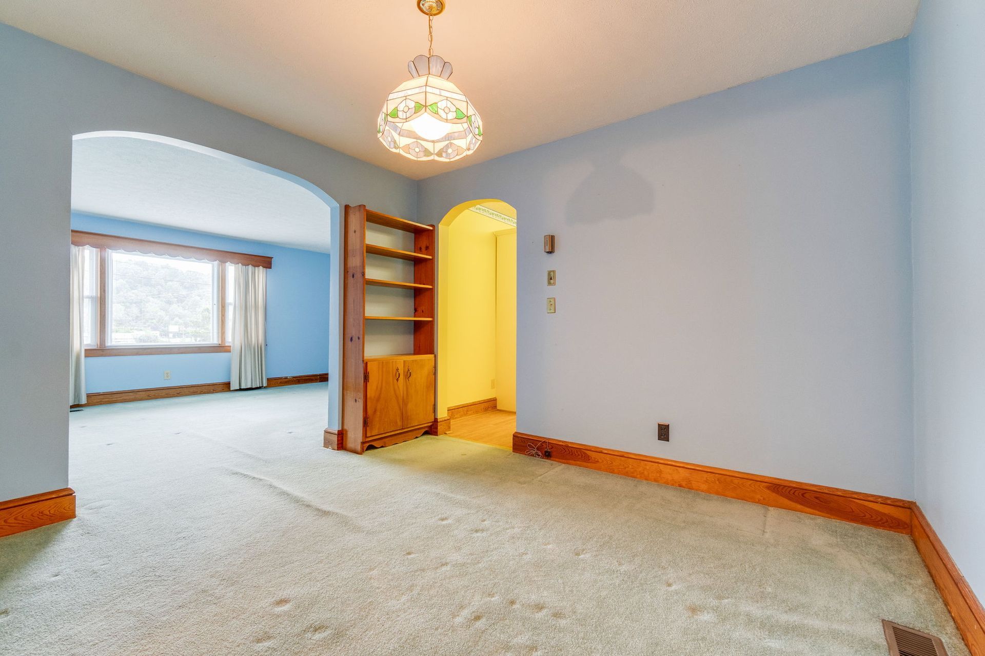 Empty carpeted room with blue walls, arched doorway, built-in shelves, and a chandelier