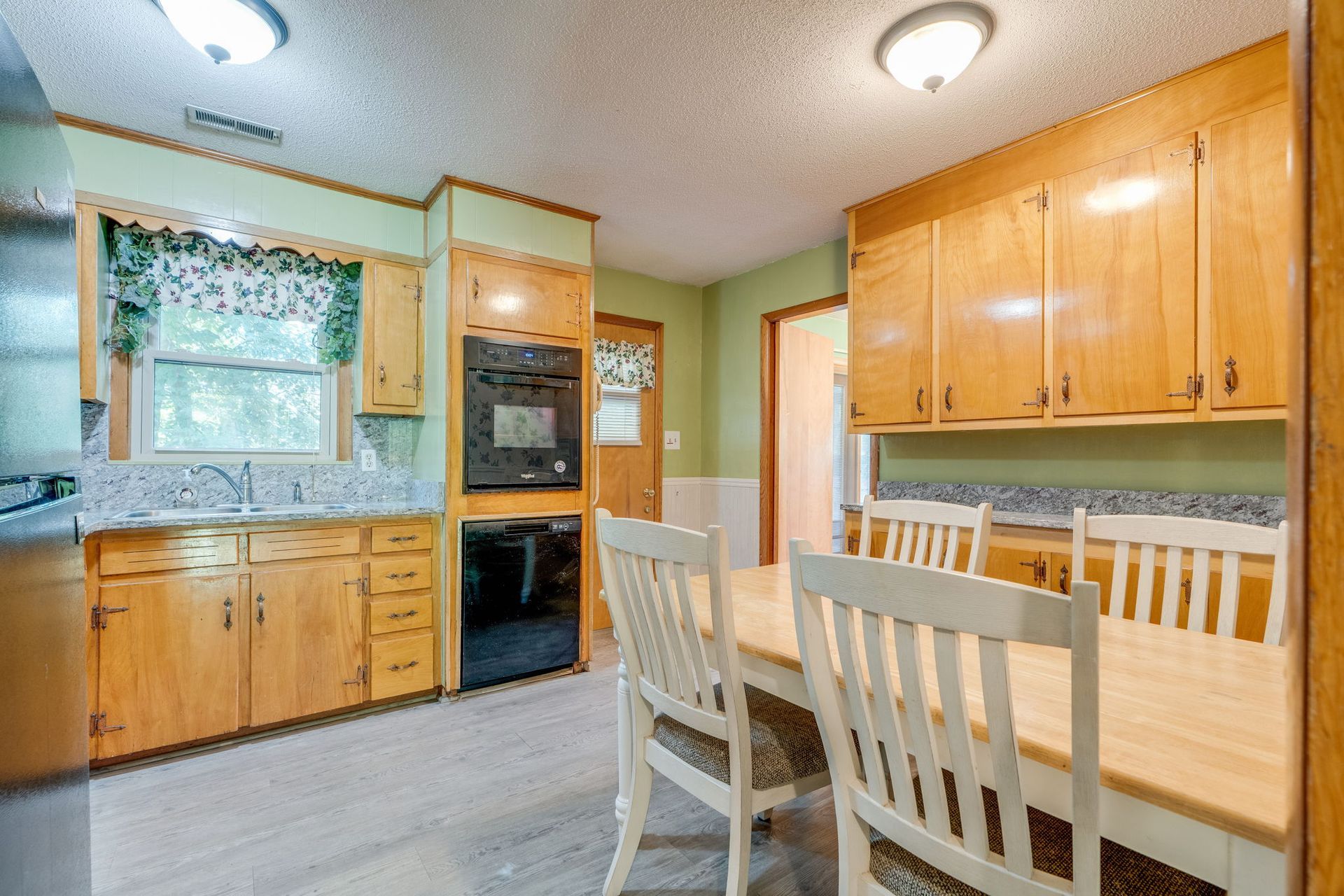 Bright kitchen with wooden cabinets, light wood dining table, and window above the sink.