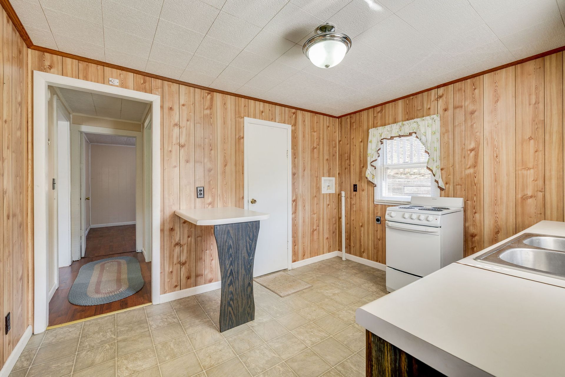 Small wood-paneled kitchen with white appliances and a doorway to a hallway