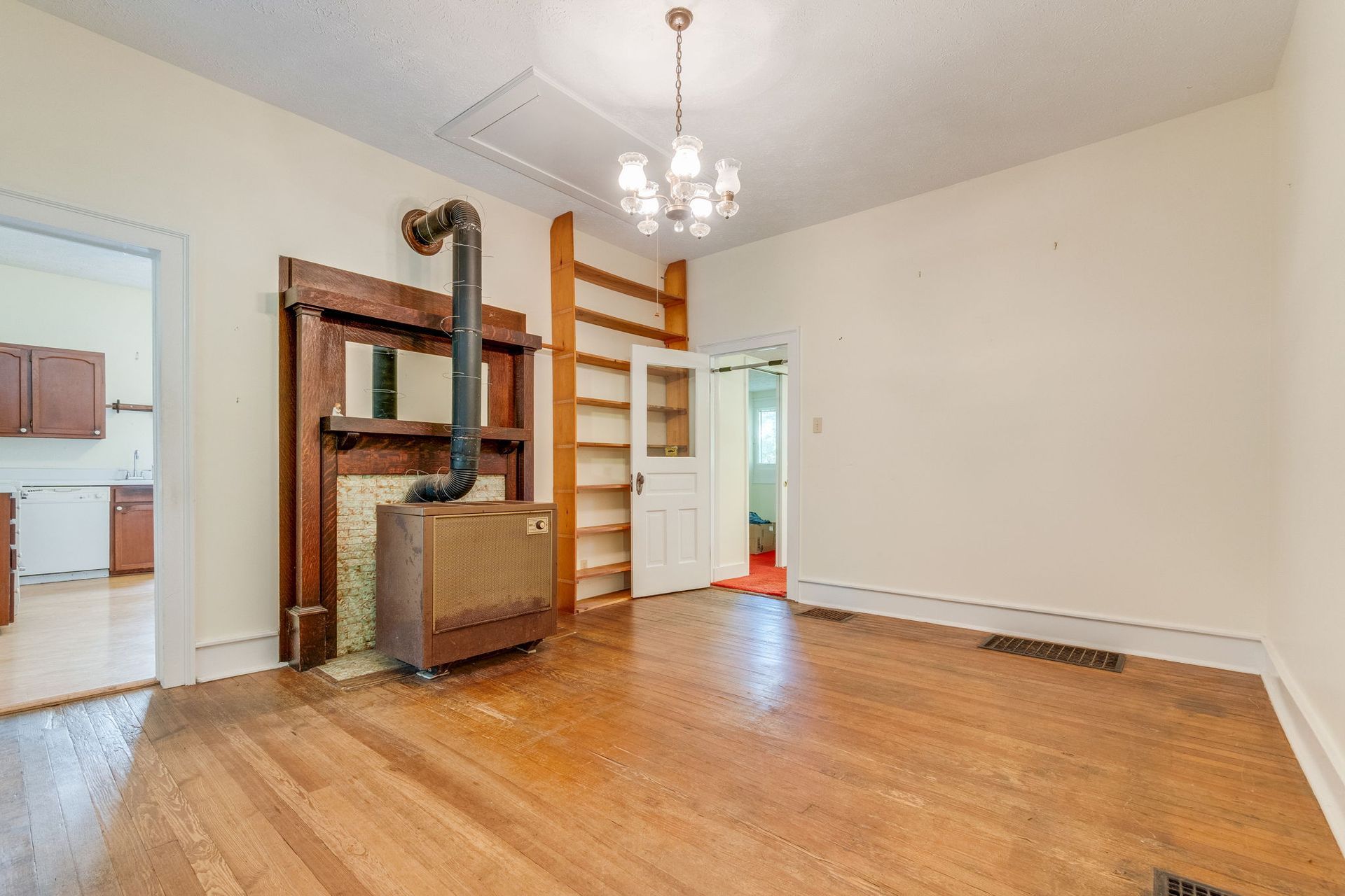 Empty living room with hardwood floors, white walls, brick fireplace, and a doorway to the kitchen