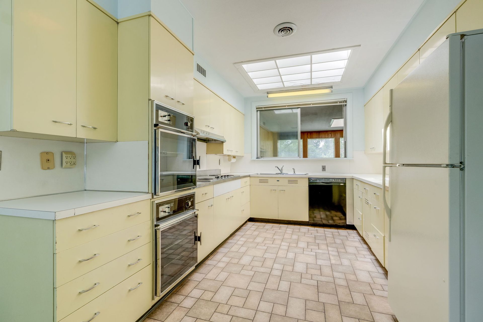 Empty retro kitchen with cream cabinets, white appliances, and tiled floor under a fluorescent ceiling light