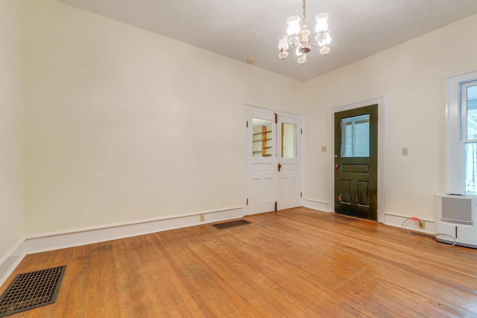 Empty room with hardwood floors, cream walls, a white door, and a dark green entry door near a window