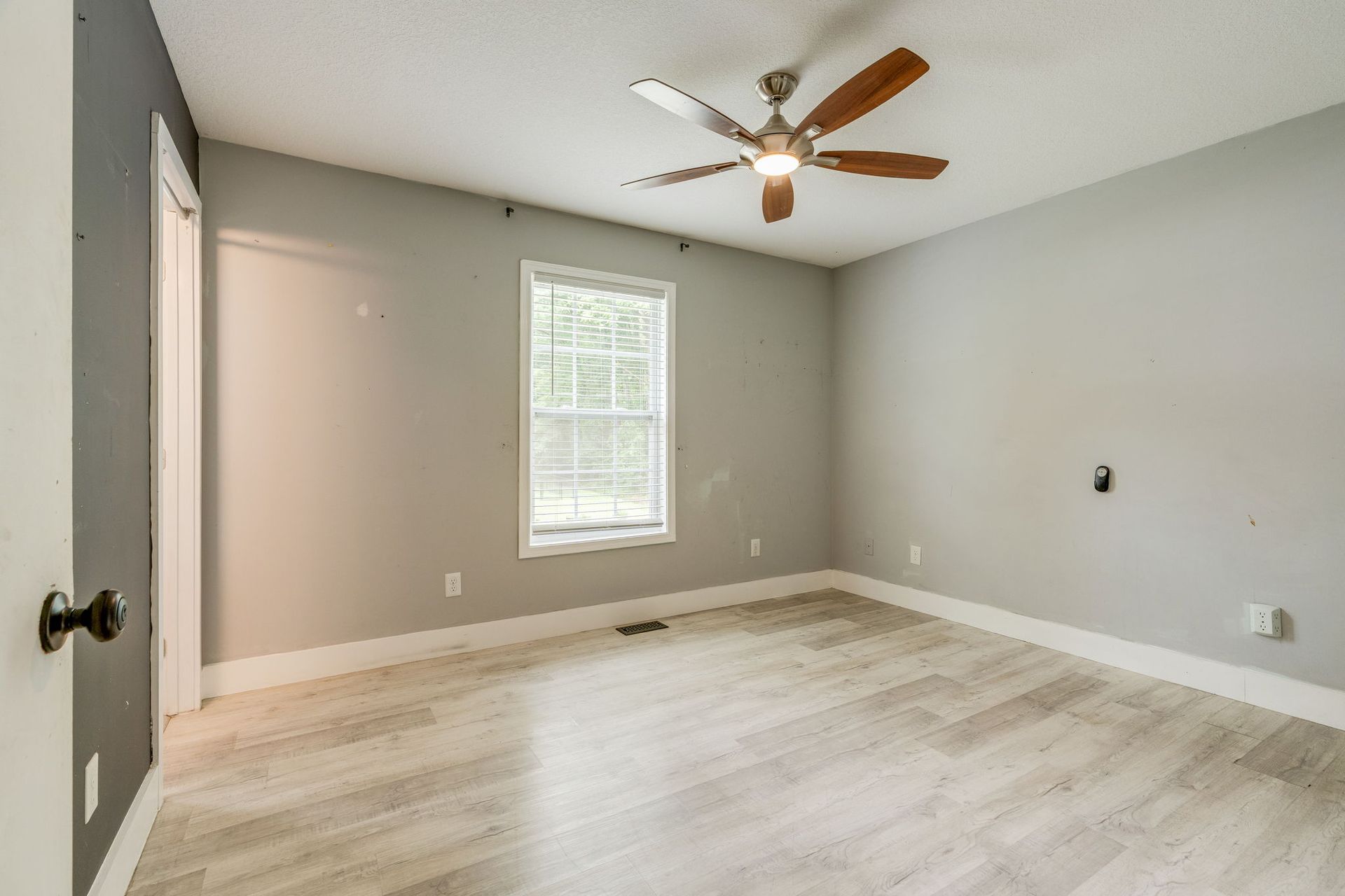 Empty beige bedroom with white trim, window, ceiling fan, and open door