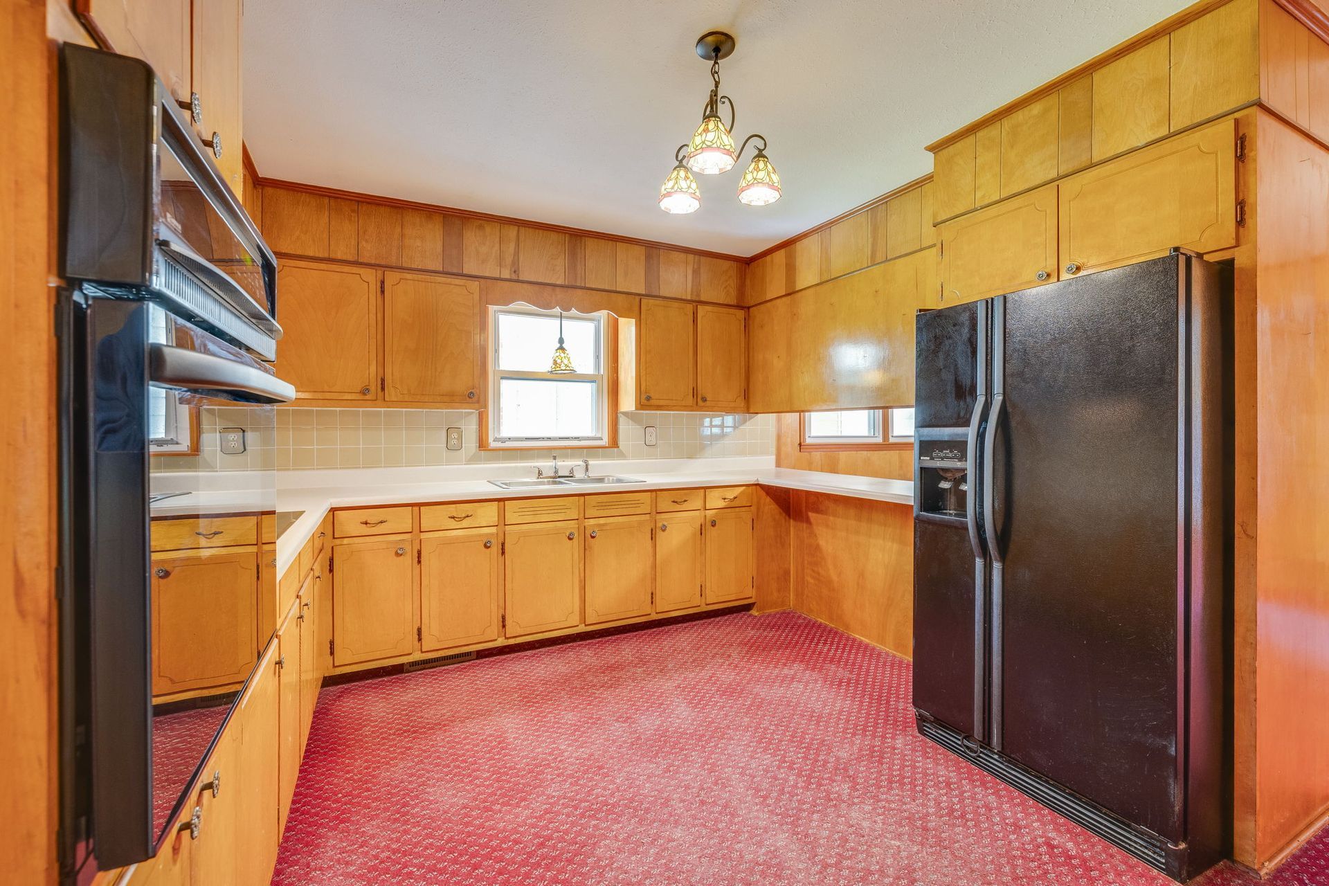 Wood-paneled kitchen with black appliances, red carpet, and a small window above the sink