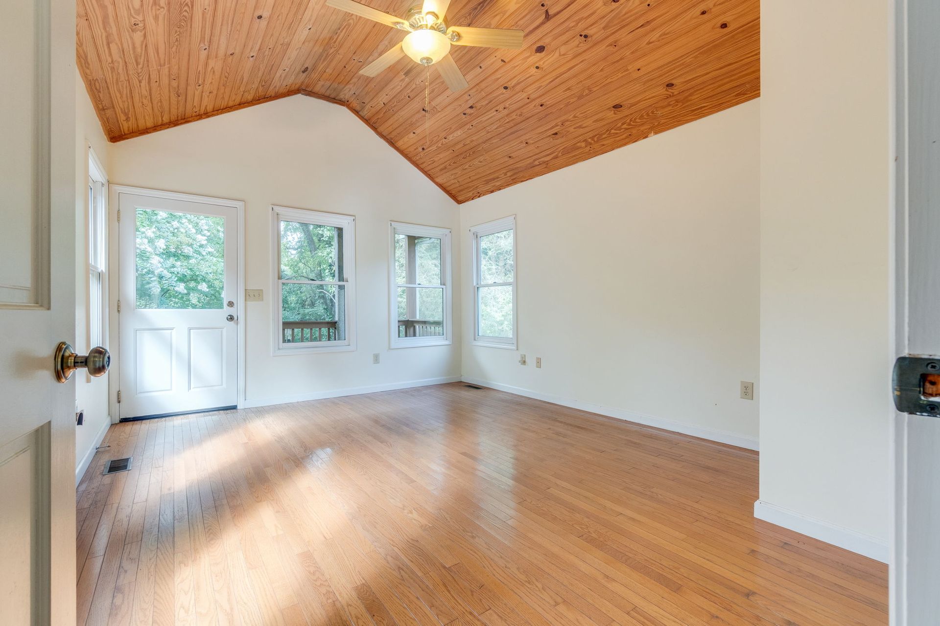 Empty room with wood ceiling, hardwood floors, and three windows beside a white door