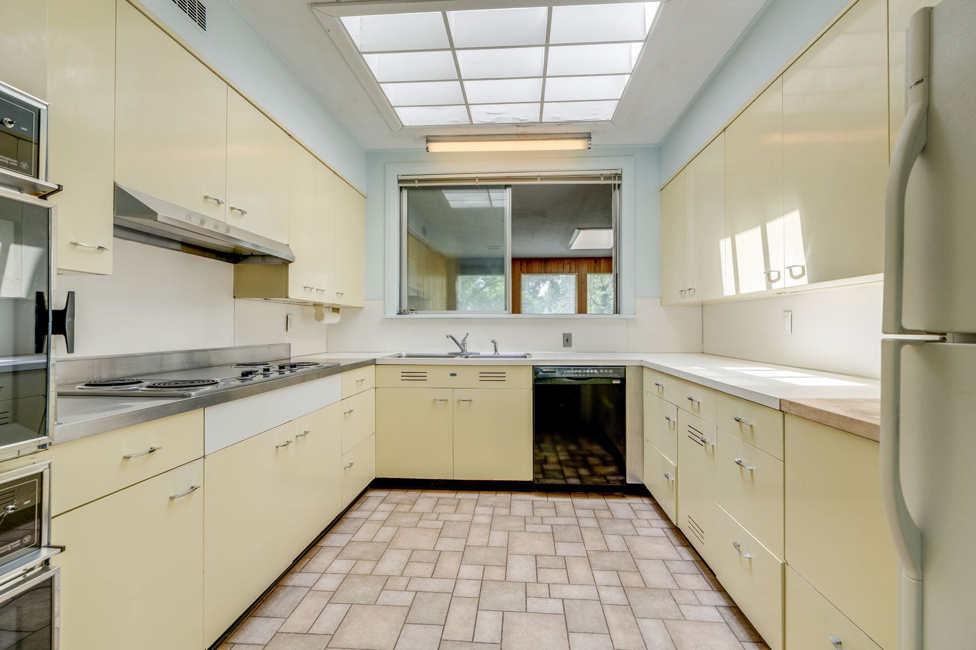 Empty cream-colored kitchen with tiled floor, white countertops, and a window over the sink.