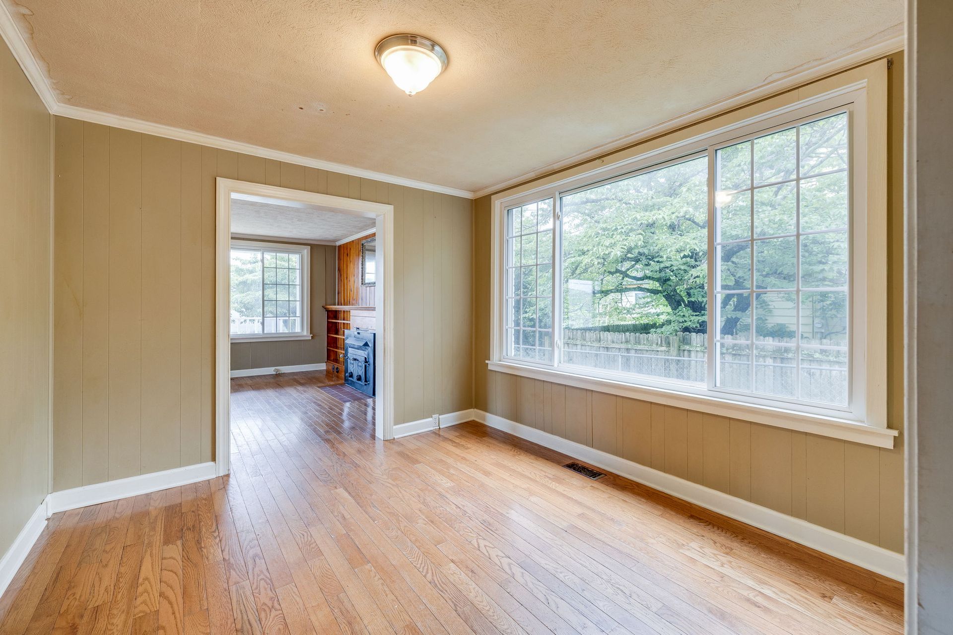 Empty beige room with hardwood floors and large windows overlooking trees
