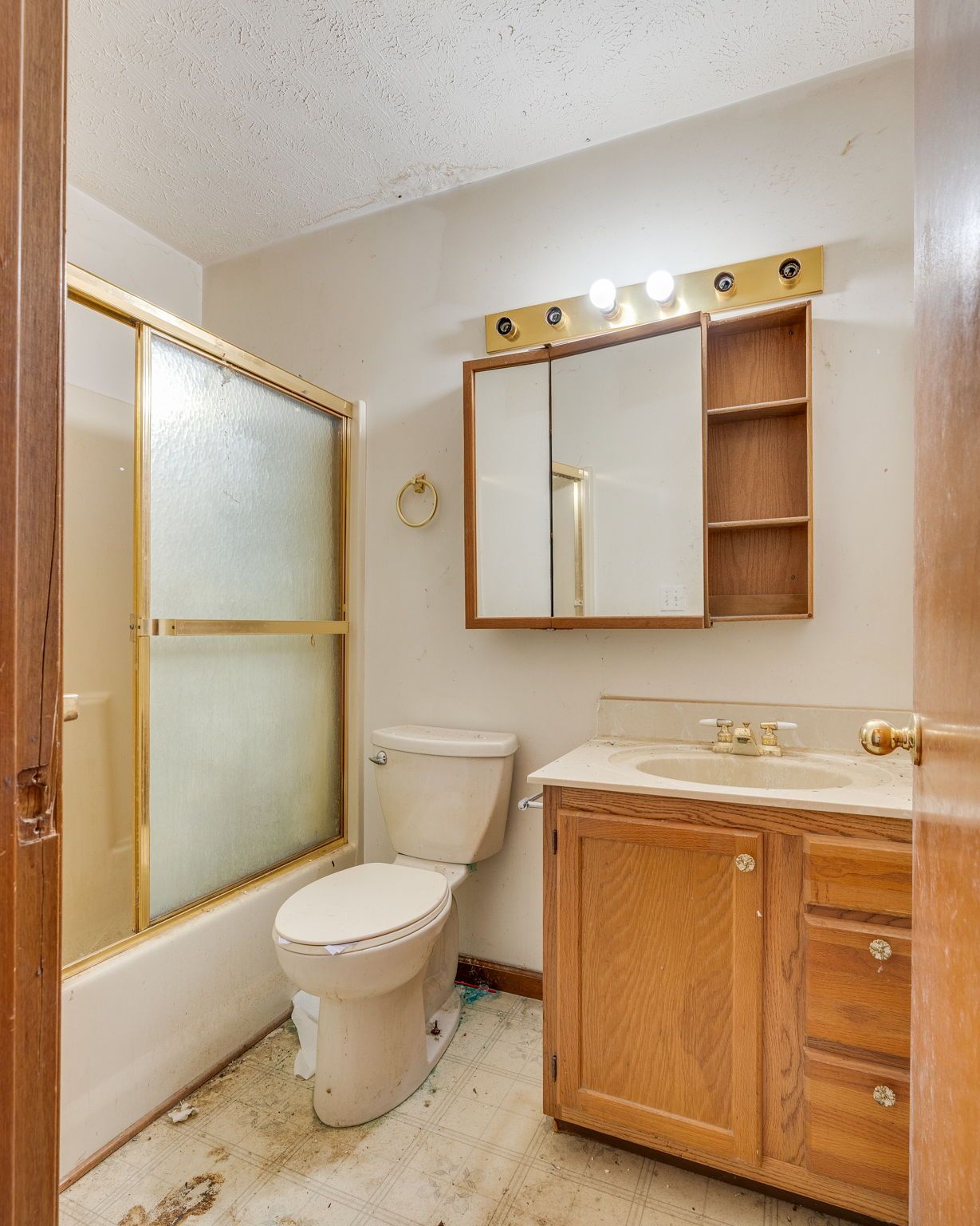 Bathroom with toilet, sink, and shower. Tan and white color scheme. Dated fixtures and flooring.