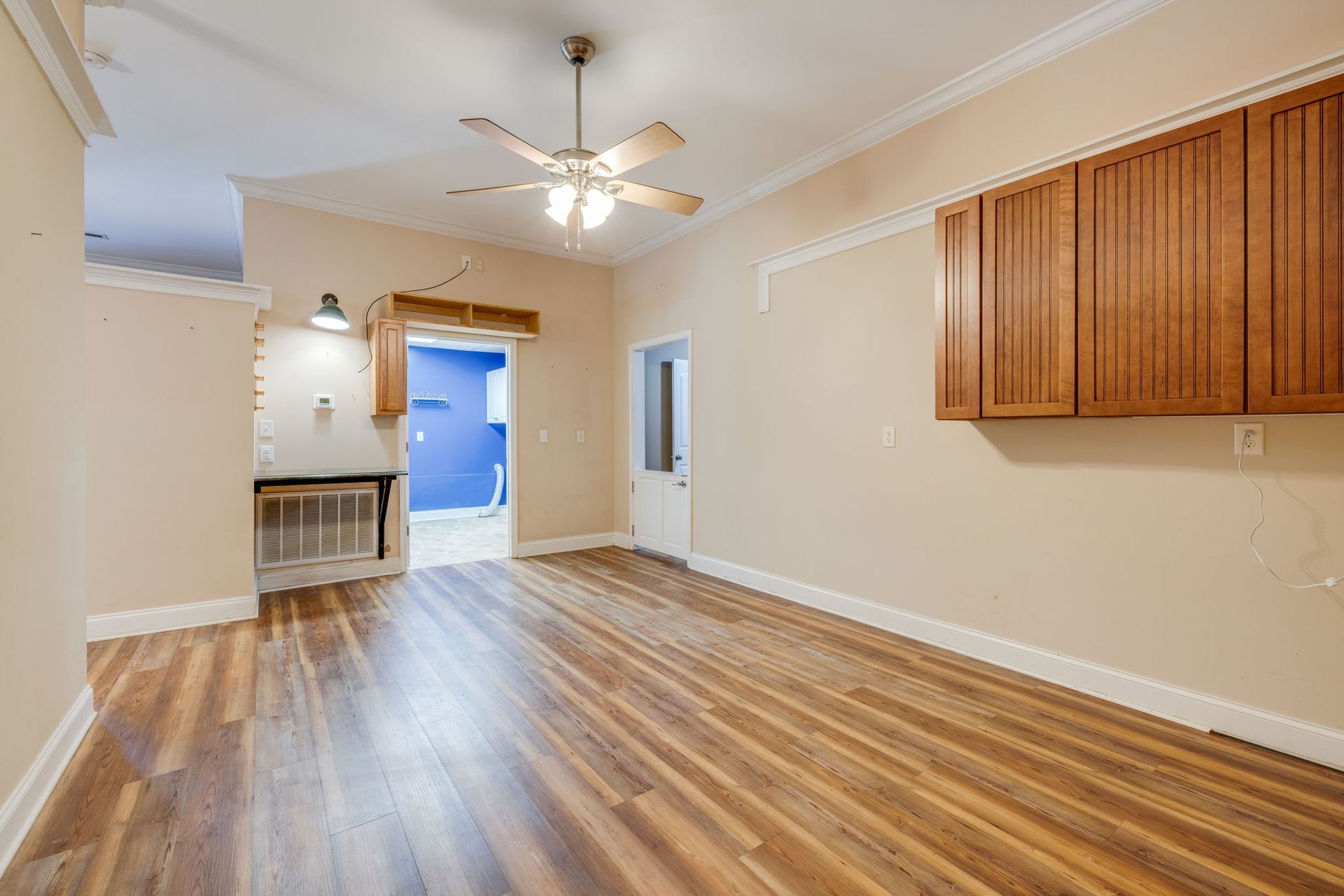 Empty beige living room with wood floors, ceiling fan, and kitchen pass-through opening