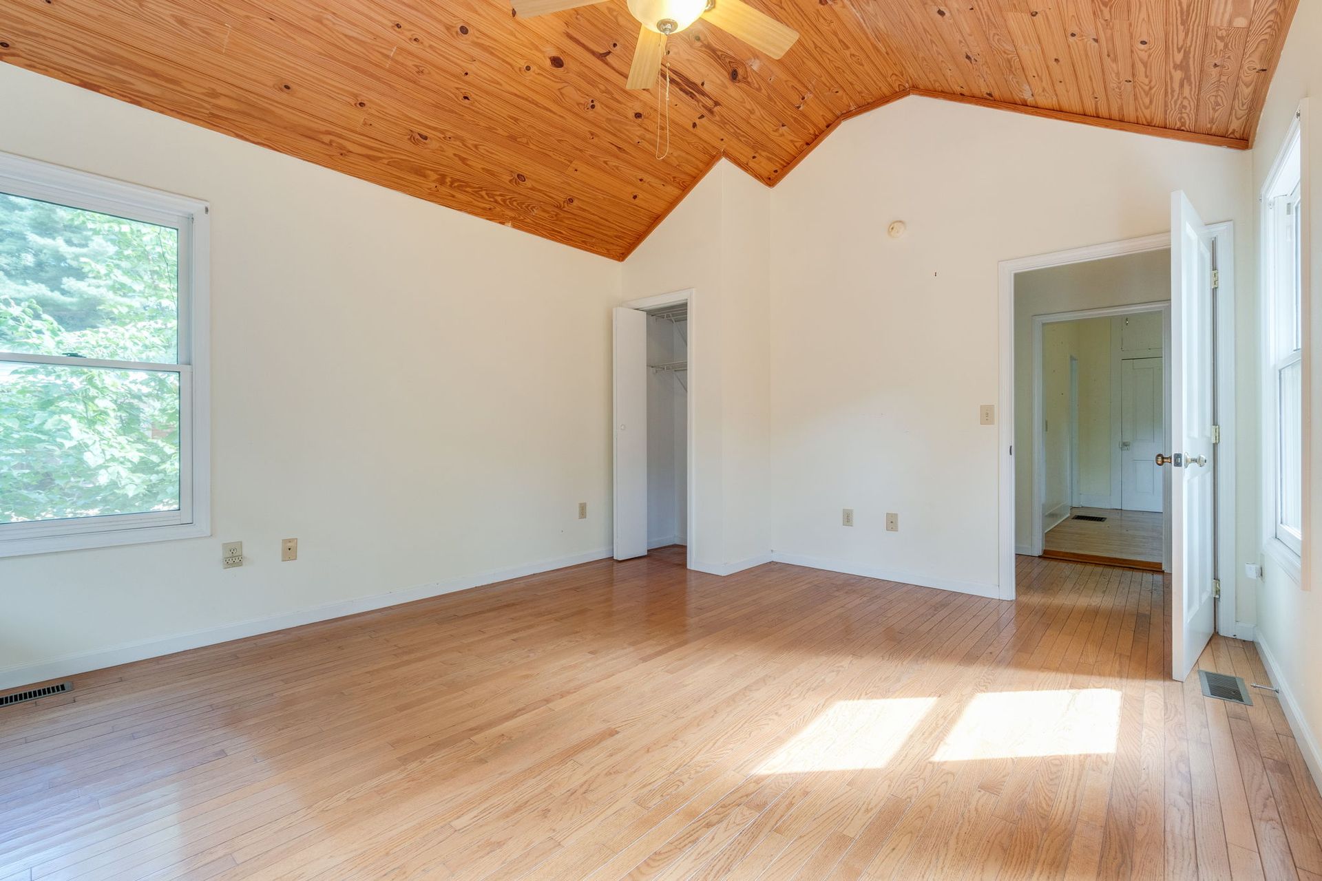 Empty room with hardwood floors, white walls, and a vaulted wood-paneled ceiling with skylights.