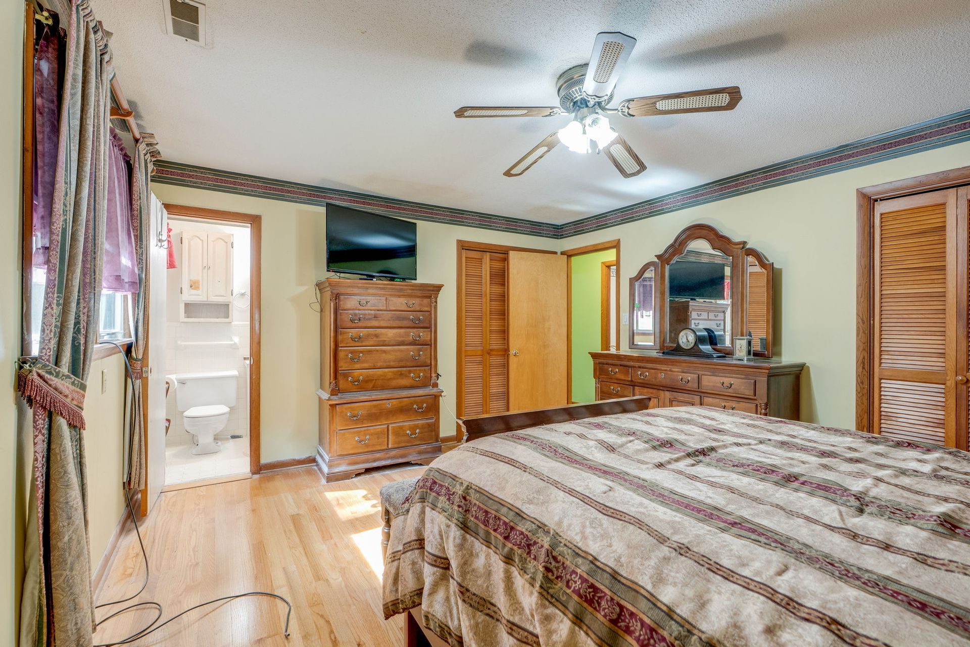 Bedroom with wood furniture, a ceiling fan, and a bathroom visible through the open doorway