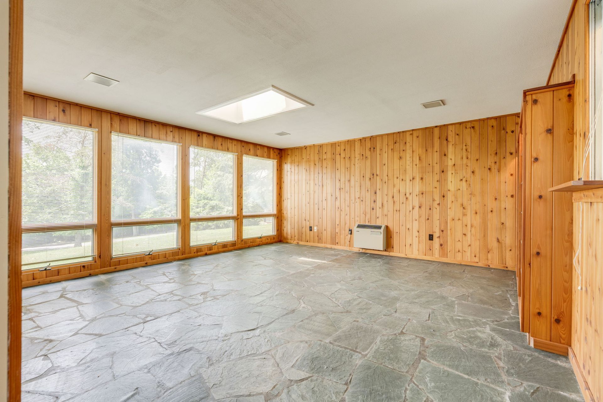 Empty room with wood-paneled walls, large windows, and a stone floor.