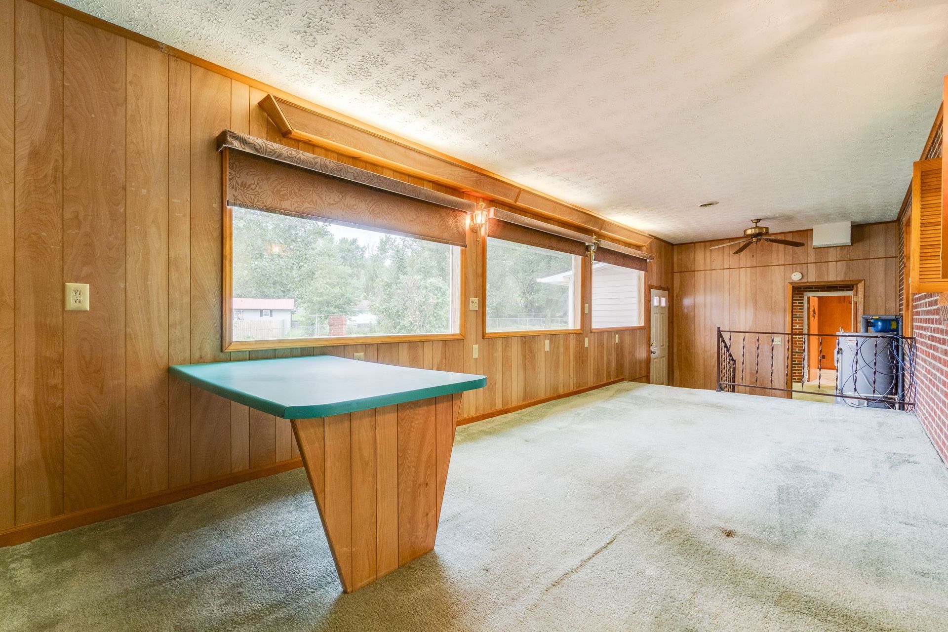 Empty wood-paneled room with large windows, beige carpet, and a built-in counter.