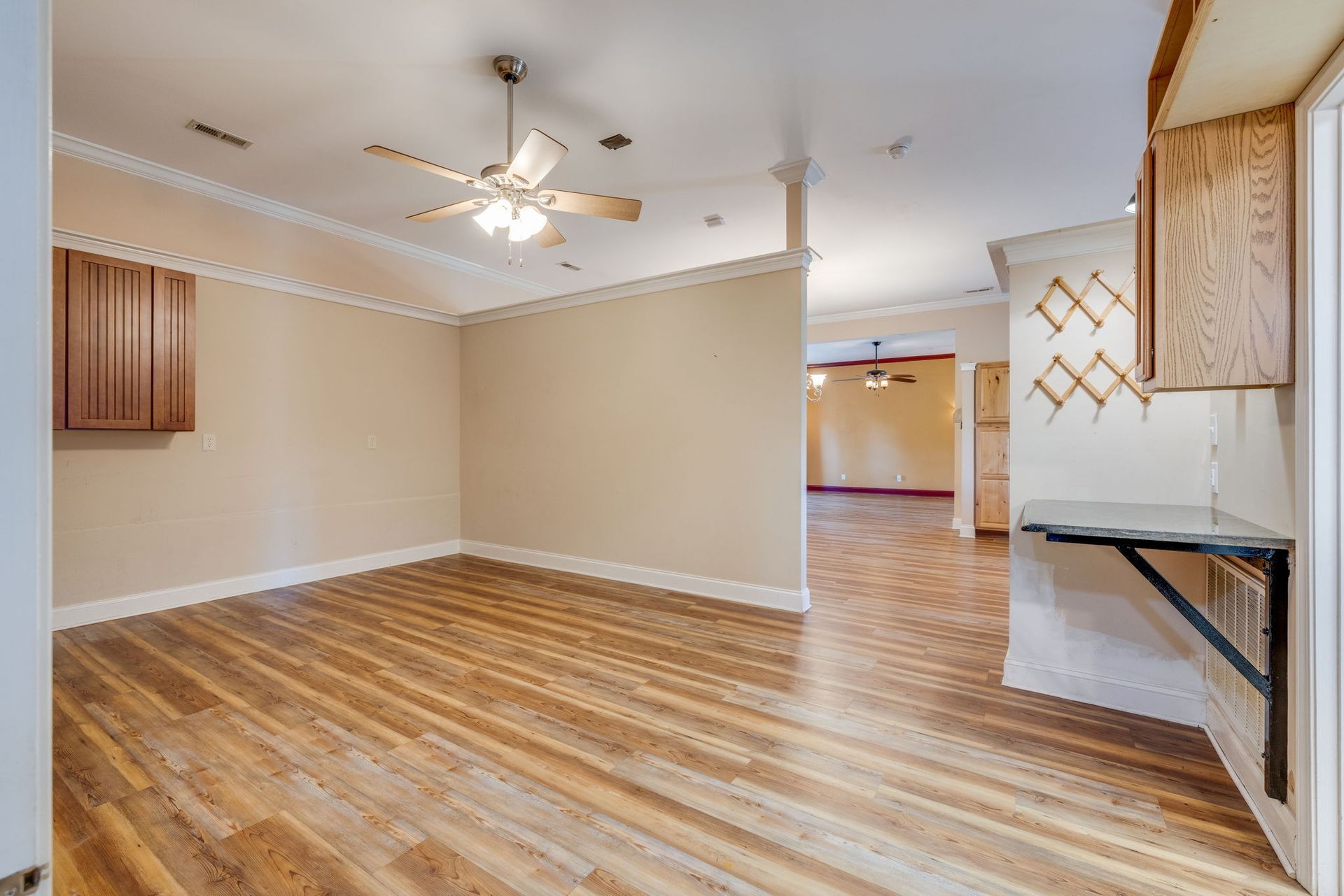 Empty room with wood floor, ceiling fan, and wall-mounted cabinets near a hallway opening.