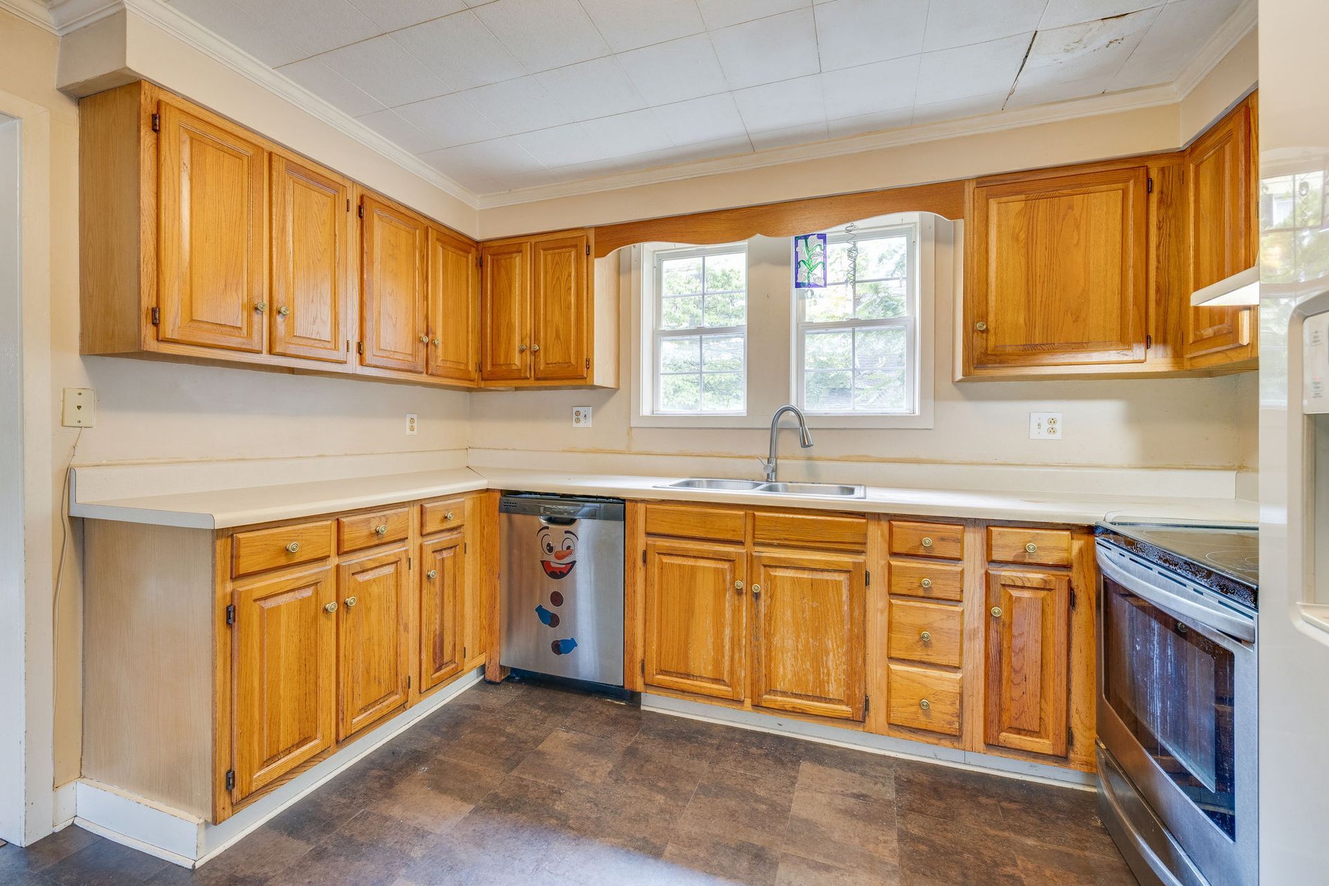 Empty kitchen with wooden cabinets, white countertops, window over sink, and a stainless-steel stove.