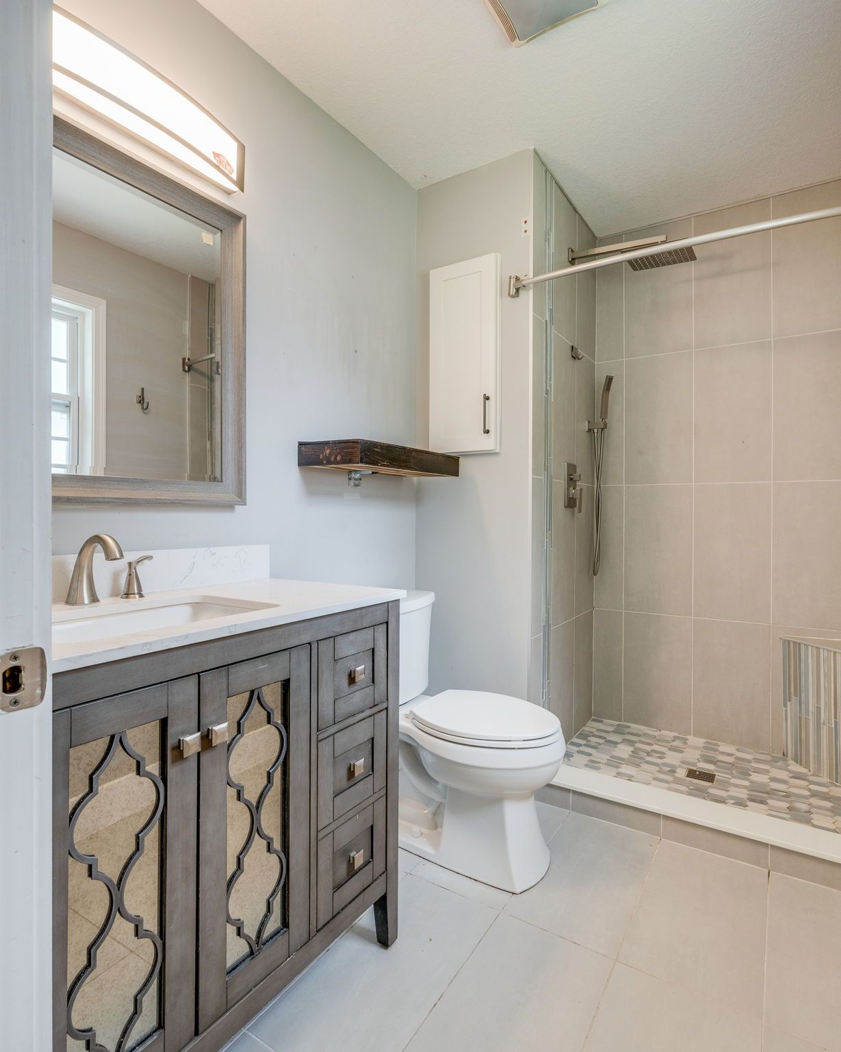 Modern bathroom with gray vanity, white sink, toilet, and glass walk-in shower