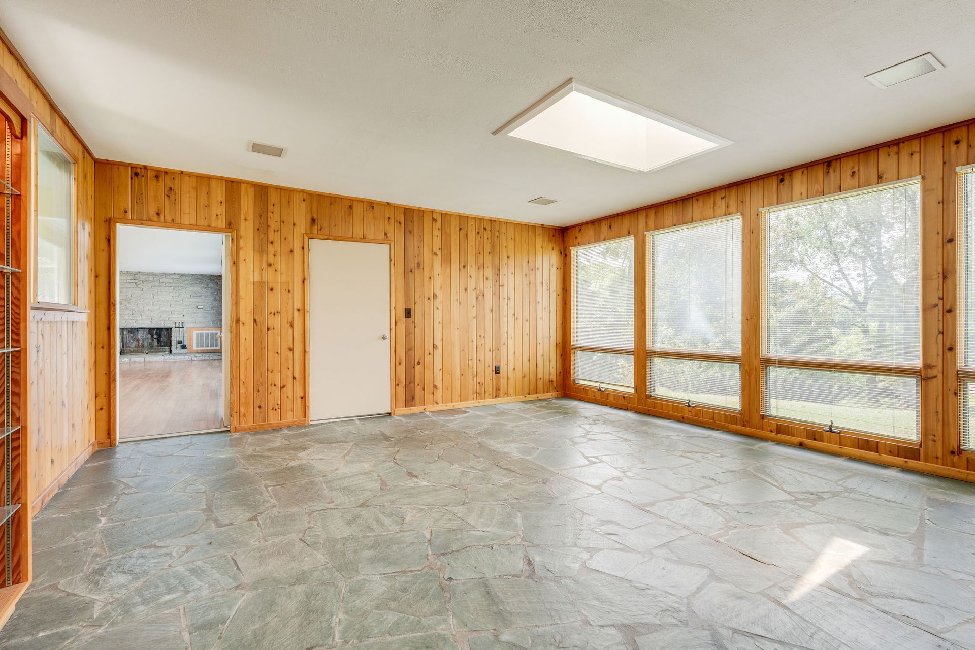 Empty sunroom with wood-paneled walls, tiled floor, and large windows letting in daylight.