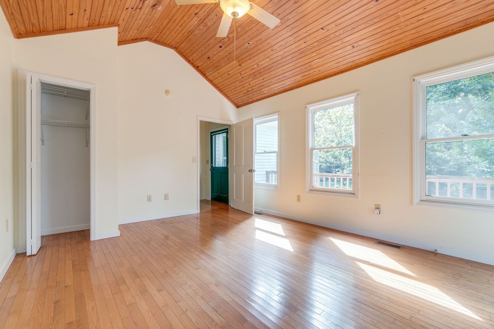 Empty room with hardwood floor, vaulted wood ceiling, ceiling fan, and sunlight through windows