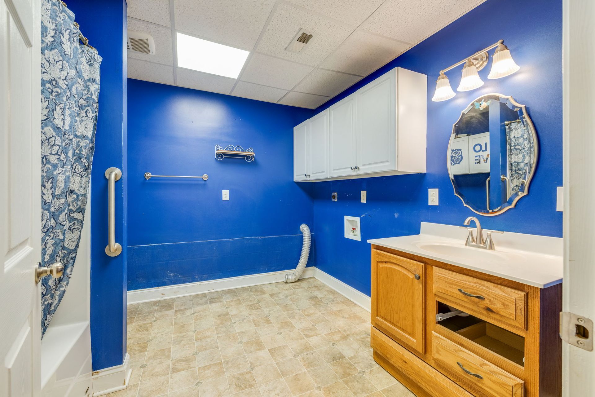Blue bathroom with white cabinets, wood vanity, mirror, and bathtub area with grab bar